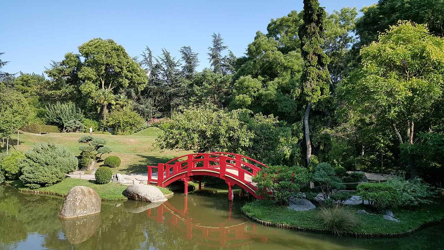 The red wooden bridge is a signature element of the park, linking the island that symbolizes the garden’s serene, meditative design.