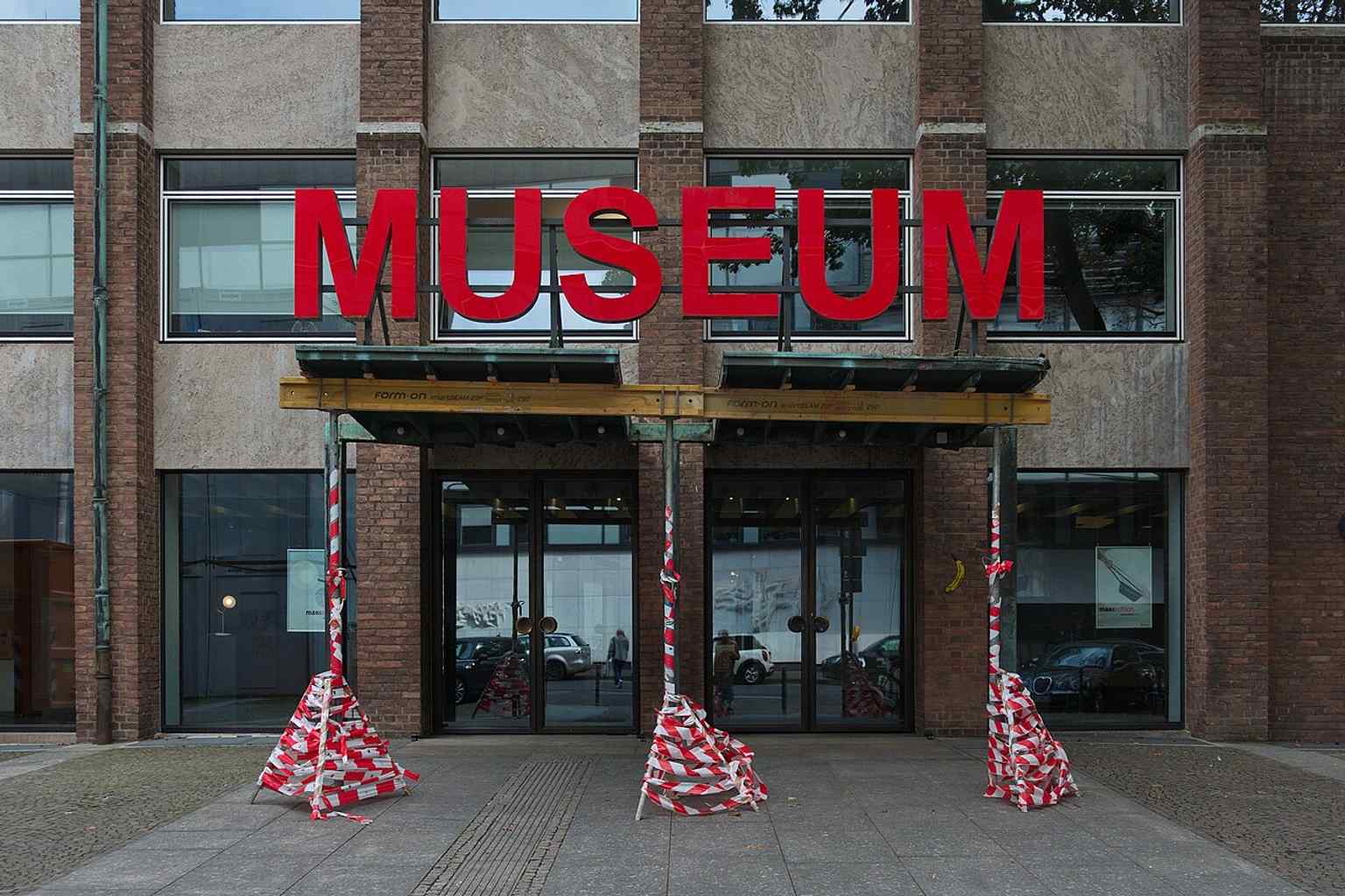 The entrance of the MAKK, located in the building originally constructed between 1953 and 1957 by Rudolf Schwarz and Josef Bernard. The exterior walls are characterized by red brick and symmetrically arranged rectangular windows.