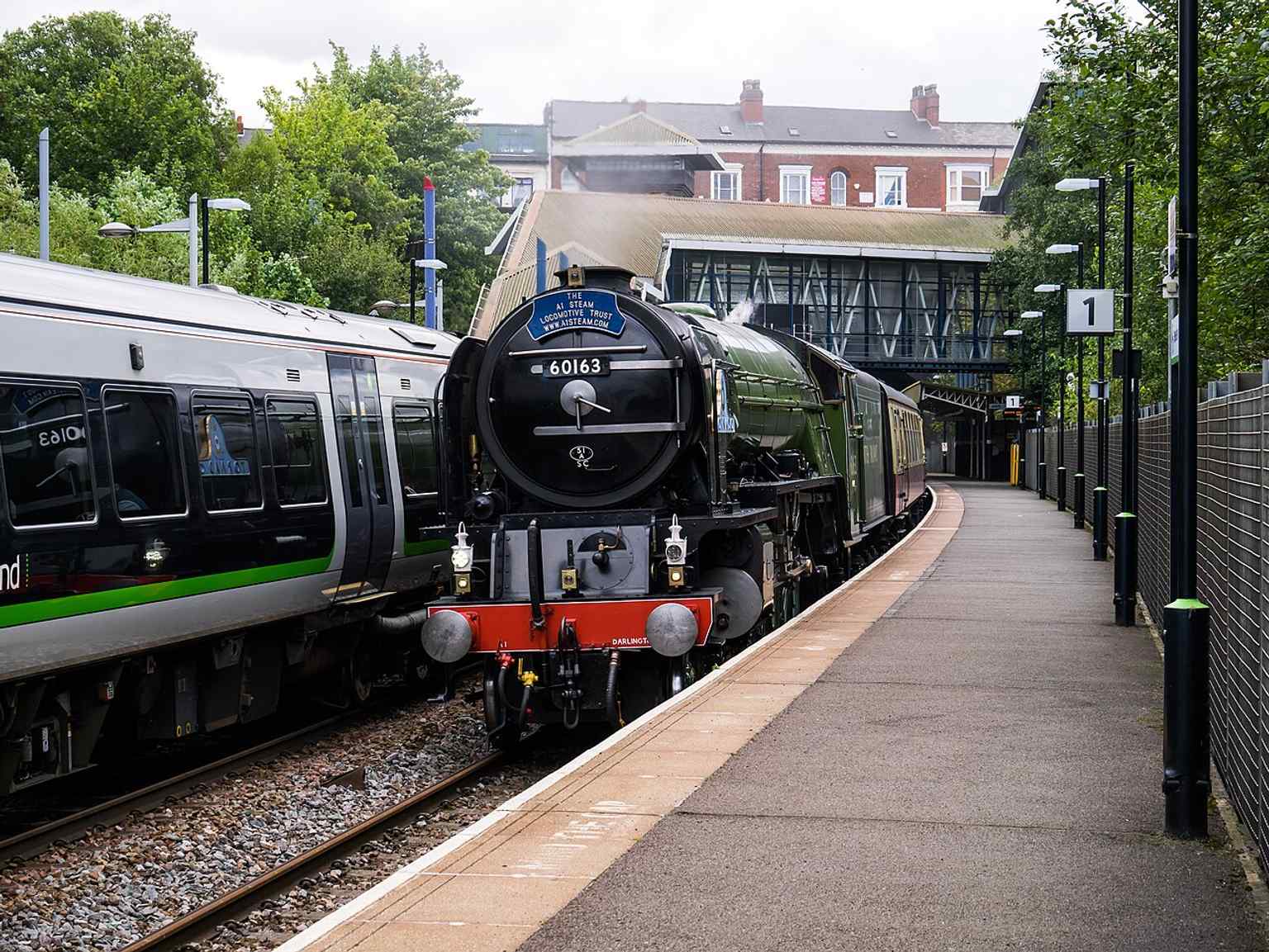 A passing London-bound steam special at the station platforms, showing the busy railway setting at this cross-city stop.