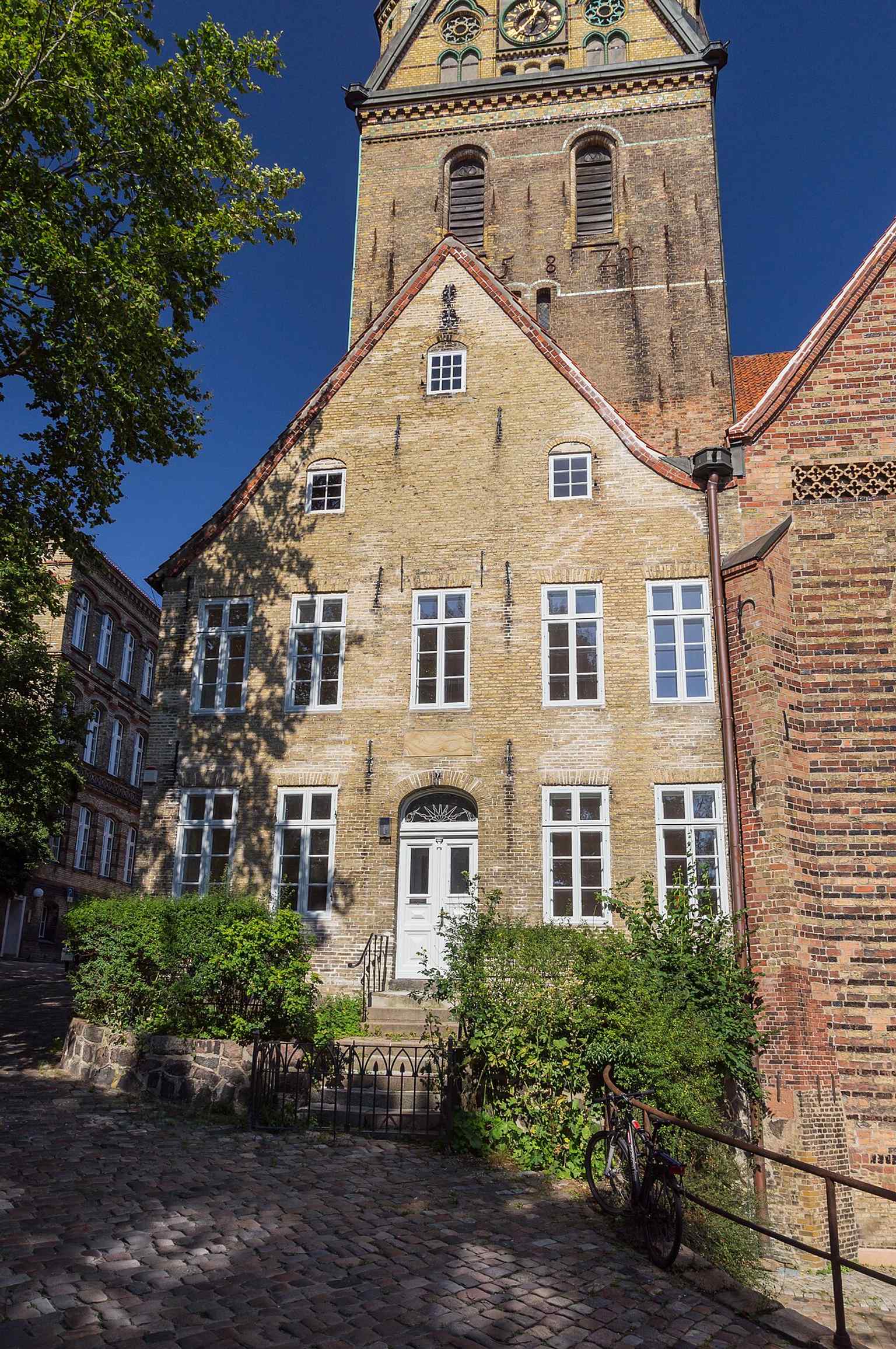 The Organistenhaus beside St. Nicholas Church — the tower rises just behind it, showing how tightly the church was woven into Flensburg’s old-town buildings.
