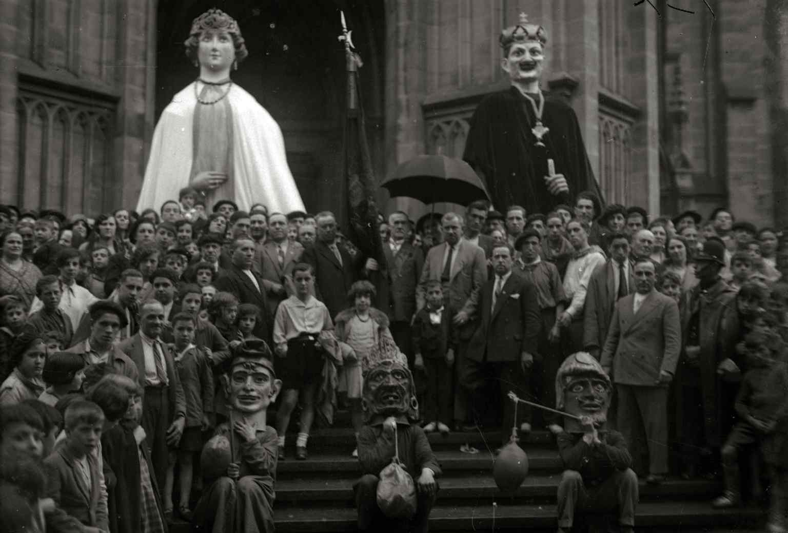 A 1930 street scene with giant parade figures outside the cathedral, capturing its role in city life, not just worship.