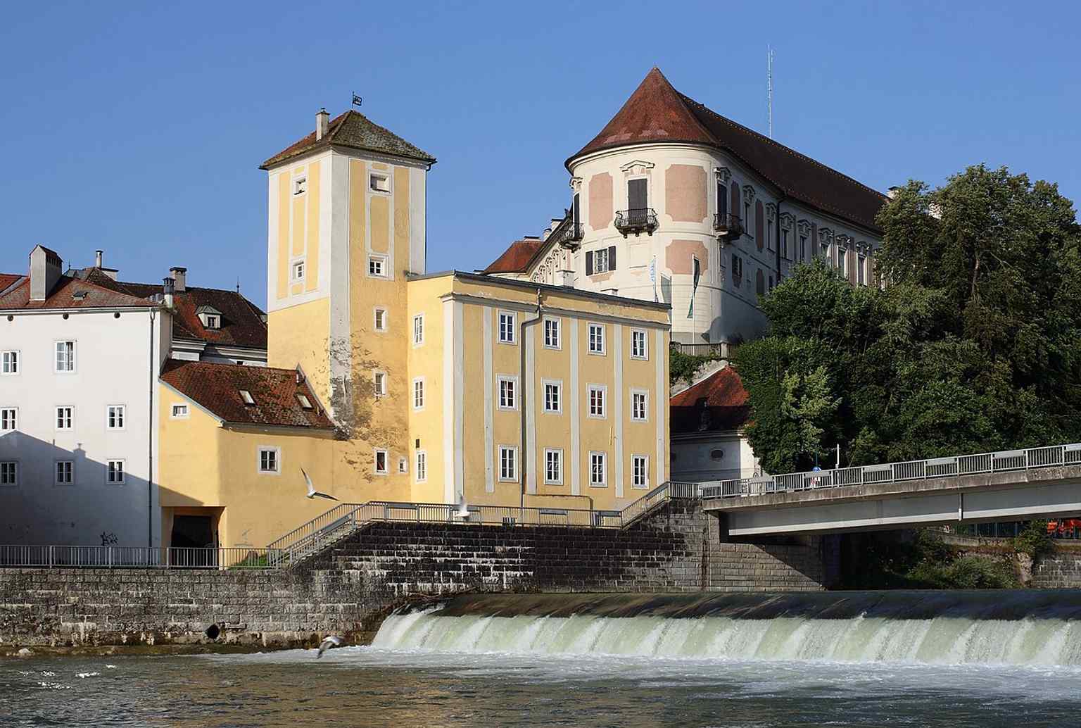 The water tower nearby helps anchor the castle within Steyr’s riverfront landscape and shows the historic urban setting around Lamberg Castle.