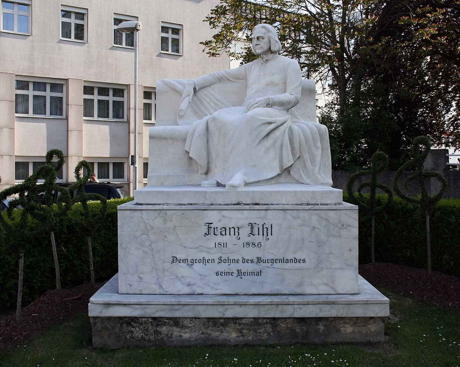 The statue’s seated figure and marble base are visible here, matching the monument described as white marble on a rectangular pedestal.