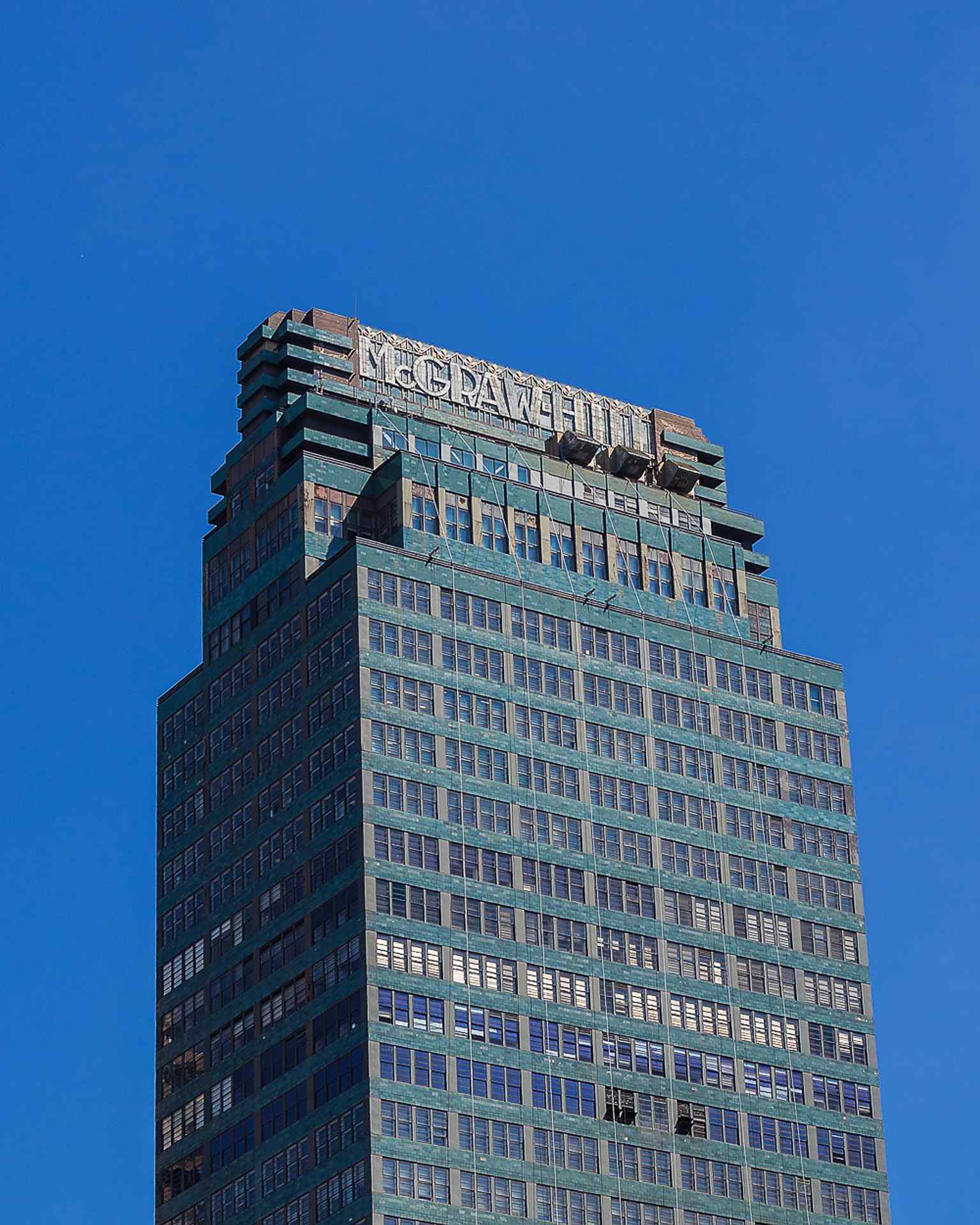 A close-up showcases the unique blue-green terracotta ceramic tile panels and green metal-framed windows, a primary means of ornament that architect Raymond Hood predicted would lead to a future skyline of "gaily colored buildings."