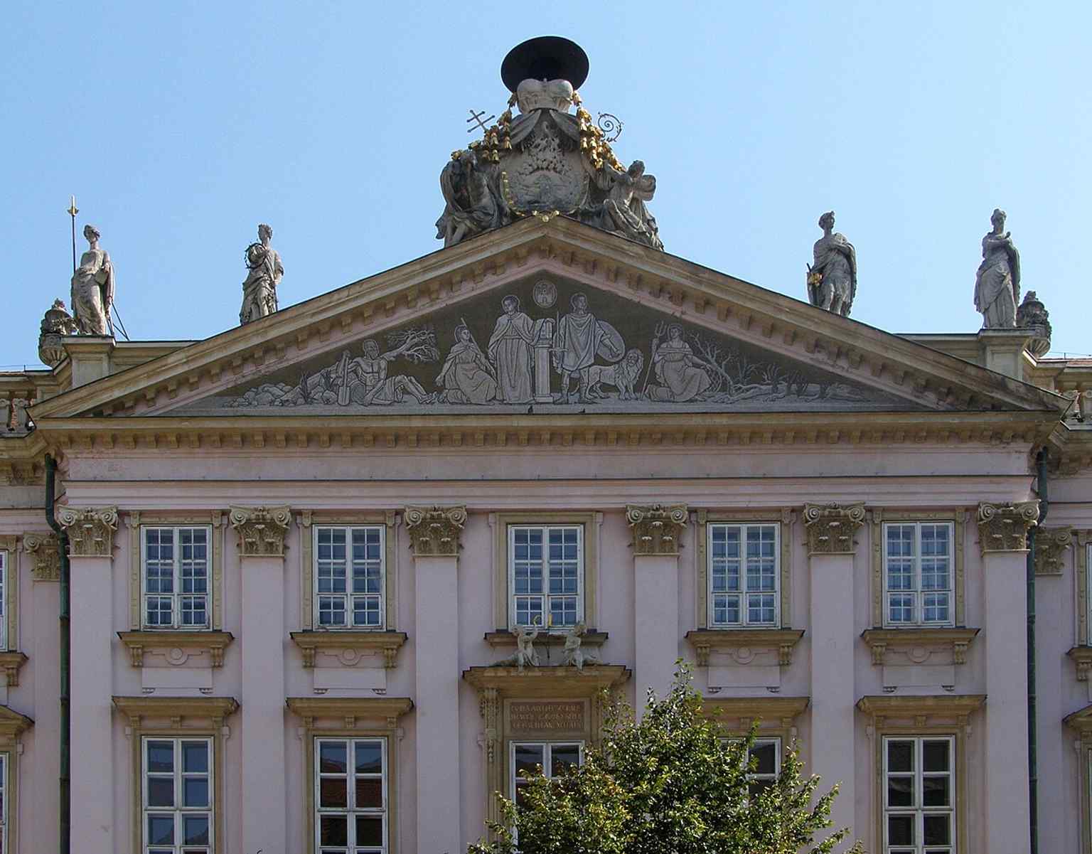 The pediment close-up highlights the palace’s classical fronton, where the original Maulbertsch fresco once crowned the façade before being replaced by a later mosaic.