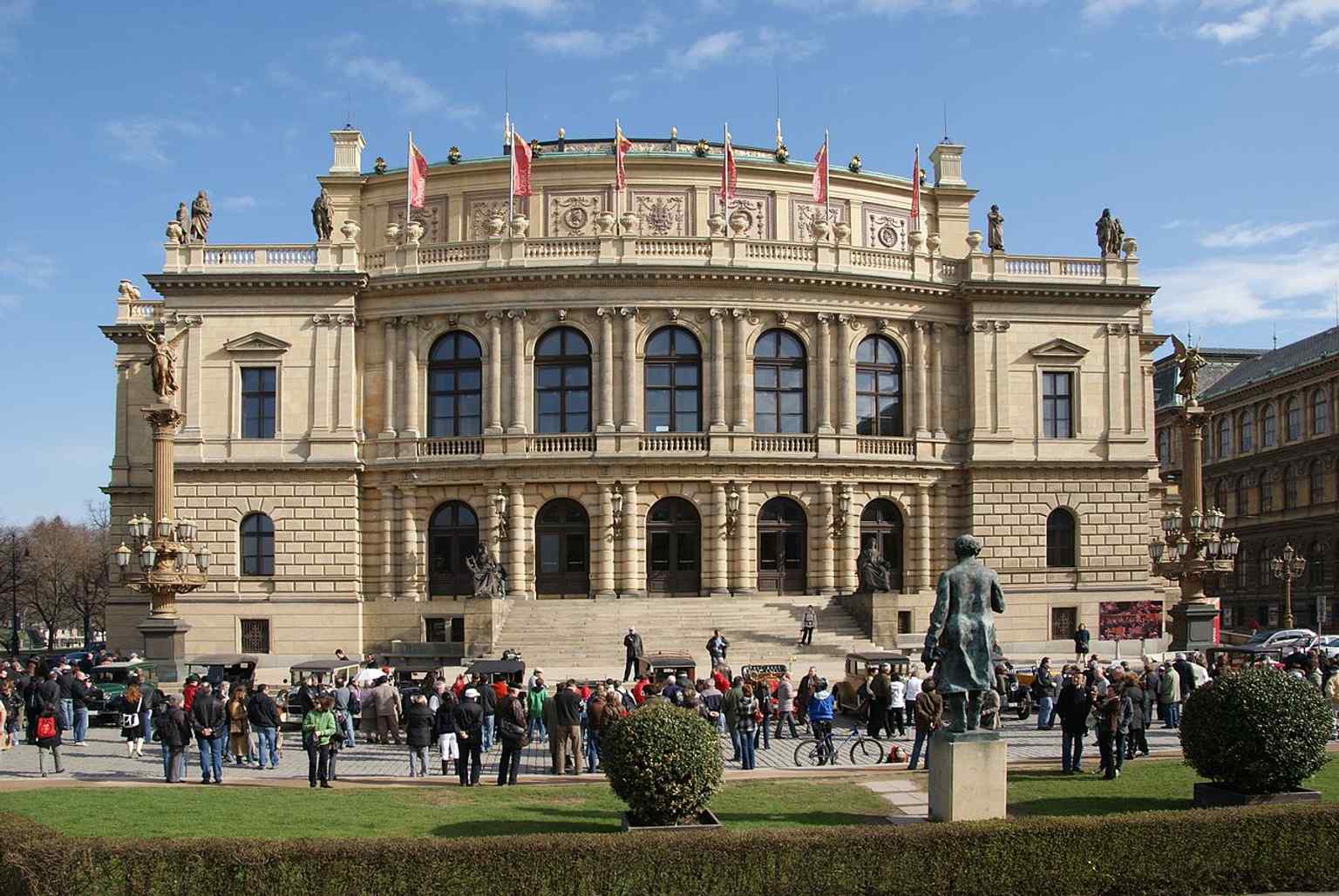 Ein malerischer Blick auf das Rudolfinum von der anderen Seite der Moldau, der seine Lage am rechten Ufer hervorhebt – ein Ort, der einst als Holzlager und Werft genutzt wurde.