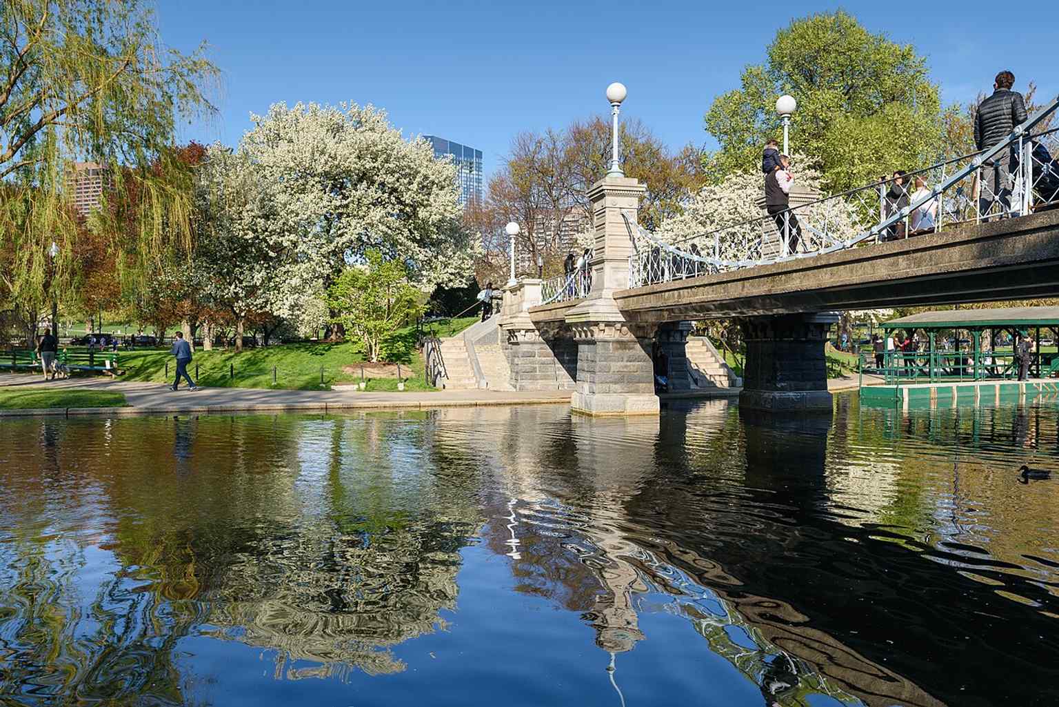 A scenic view of the pond and footbridge captures the garden’s winding paths and English landscape-garden style.