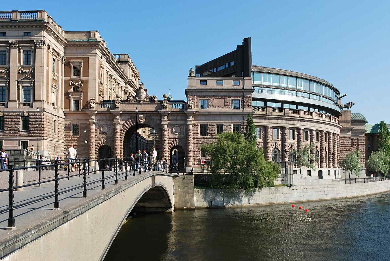 Walking toward the building along Riksbron emphasizes the approach to the parliament house across the water, just as visitors experience it on foot.
