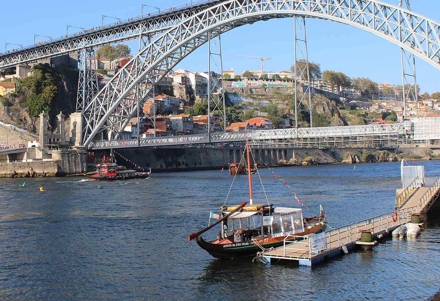 Boats passing beneath the bridge underline the Douro crossing that originally replaced the old suspension bridge and transformed river traffic.