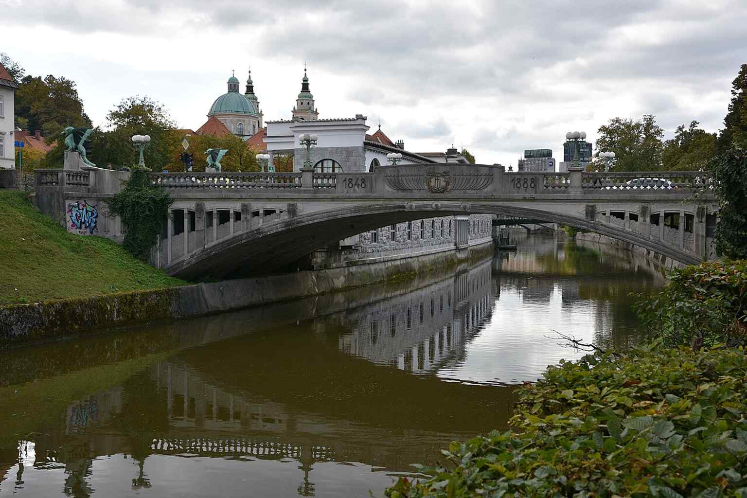 The Dragon Bridge elegantly crosses the Ljubljanica River in Ljubljana, a key part of Mayor Ivan Hribar's vision for a 'new Ljubljana' built in the latest artistic styles after the 1895 earthquake.
