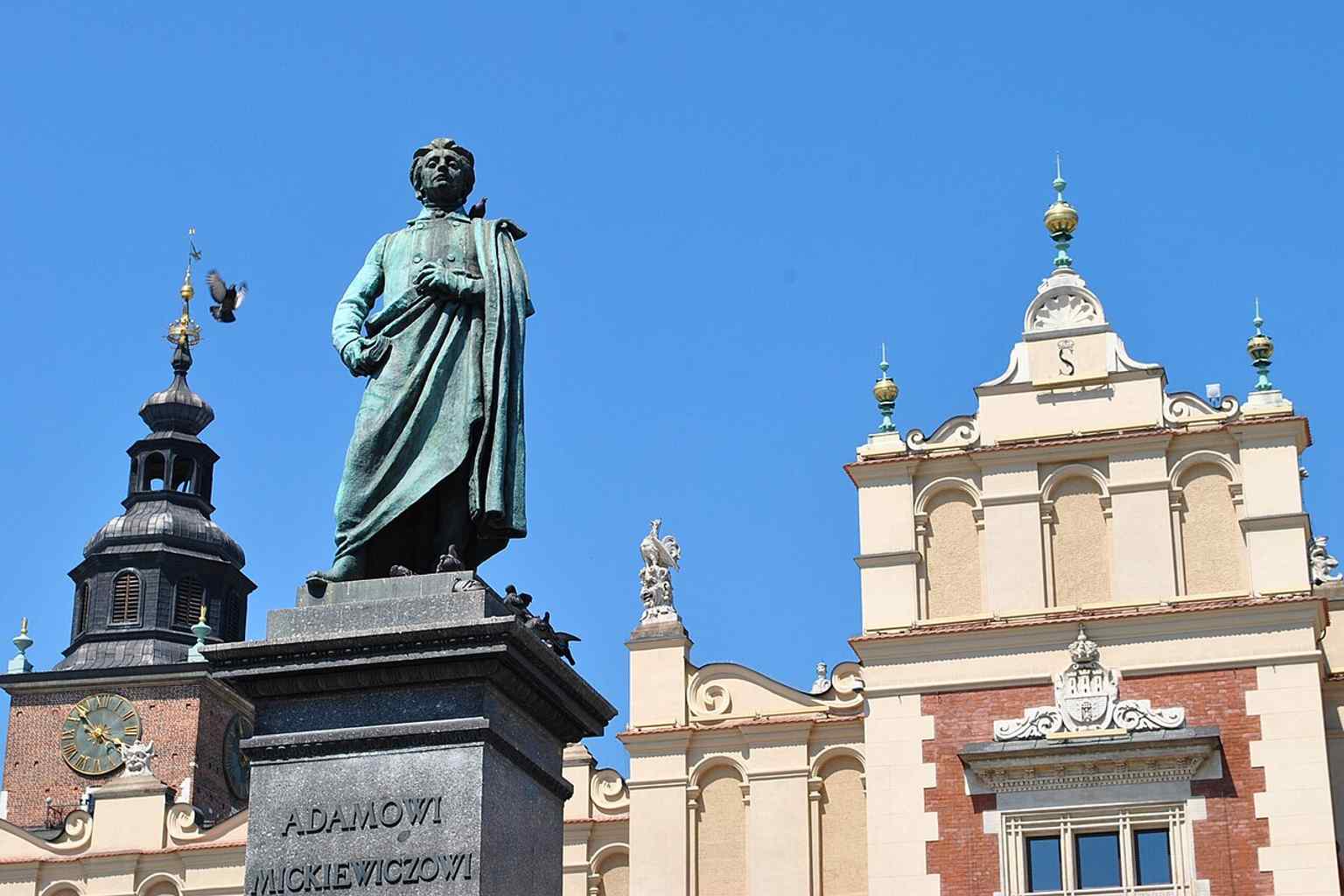 Mickiewicz in the square with the Sukiennice in the background — a classic view of the landmark in its busiest, most iconic setting.