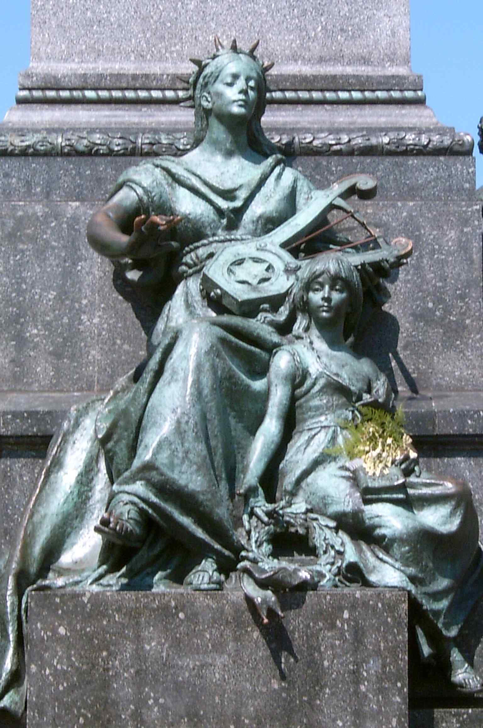 A straightforward full view of the monument, ideal for introducing the poet statue and the four allegorical figures at its base.