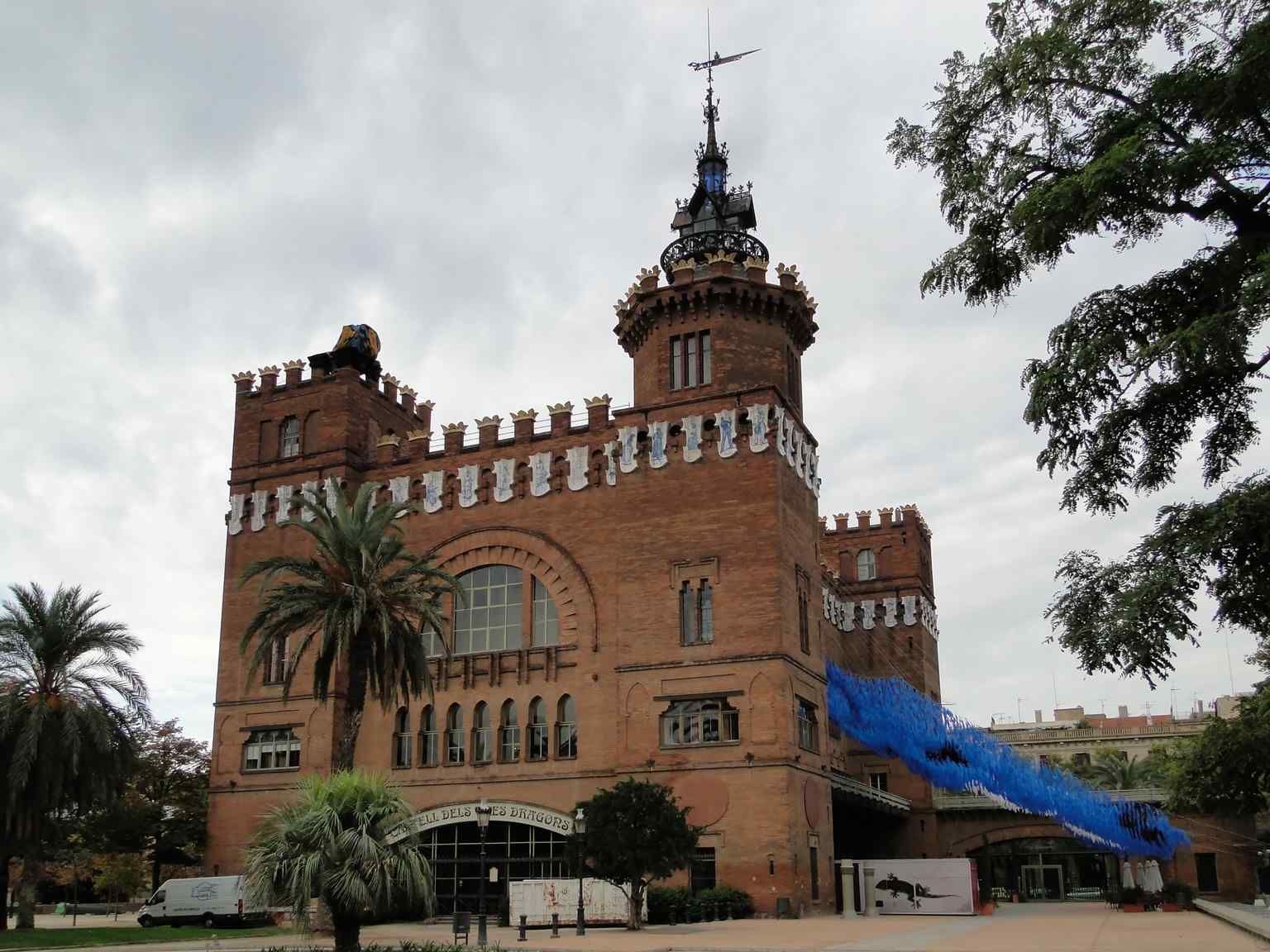 This view captures the striking modernist architecture of the Castle of the Three Dragons, built with visible brick and iron, featuring battlements and a castle-like design.