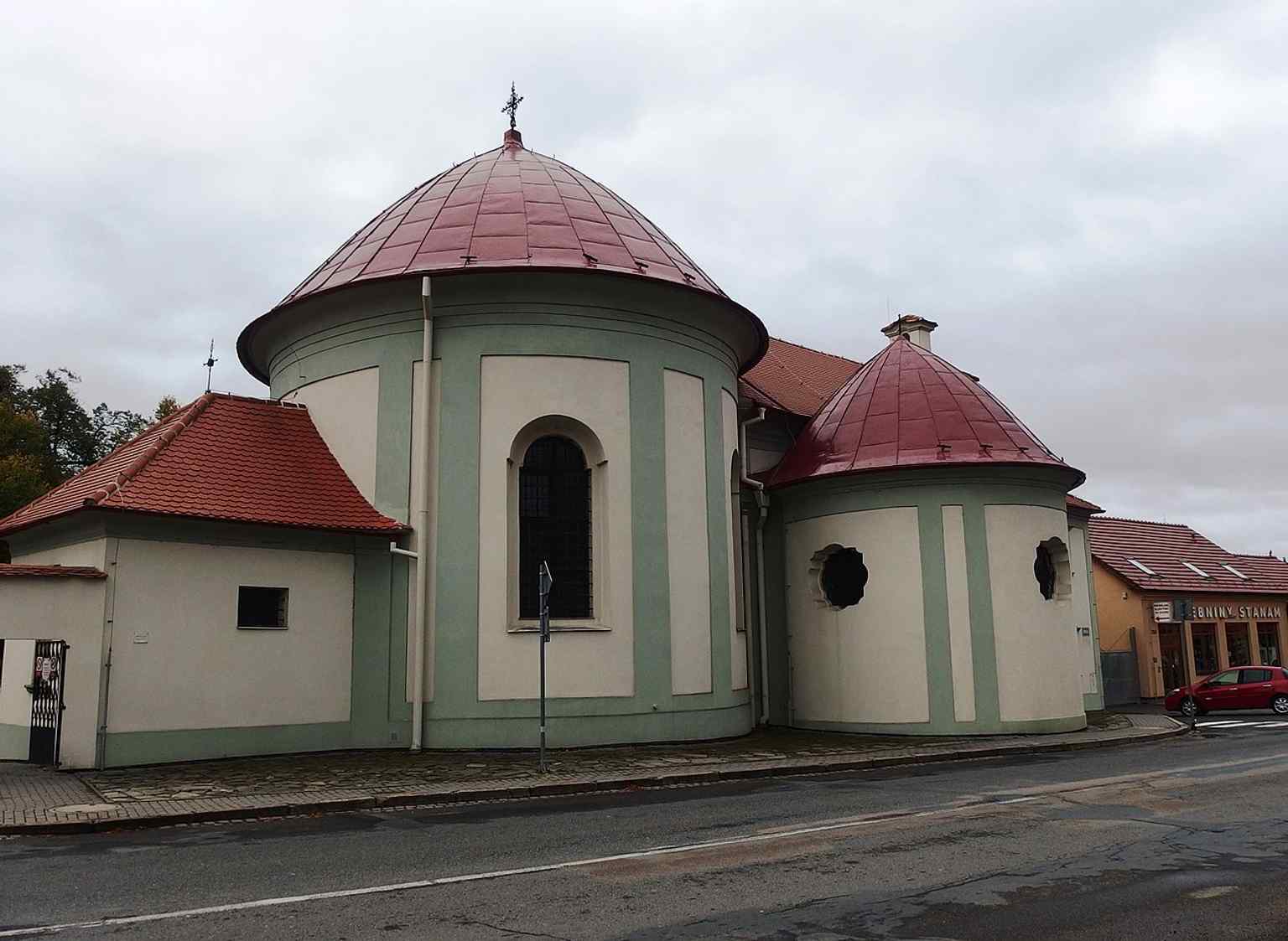 The Neoclassical cemetery gate, built much later than the chapel, features a segmentally arched entrance topped with a hand-beaten metal figure of Jesus on a cross.