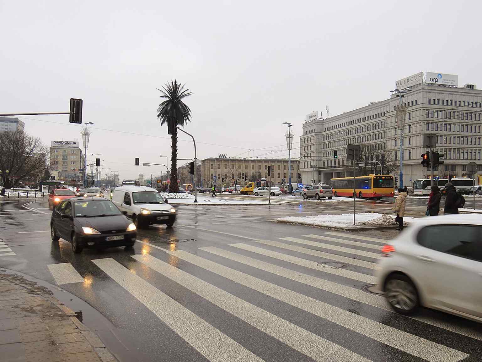 A broad overhead-style city view of the roundabout, showing how the palm anchors this busy central Warsaw junction.
