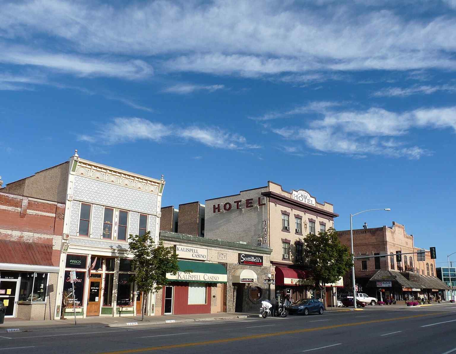 A streetscape of Main Street showing the Brewery Saloon, Kalispell Grand Hotel, and McIntosh Opera House — three buildings that helped define the district’s late-1890s boomtown era.