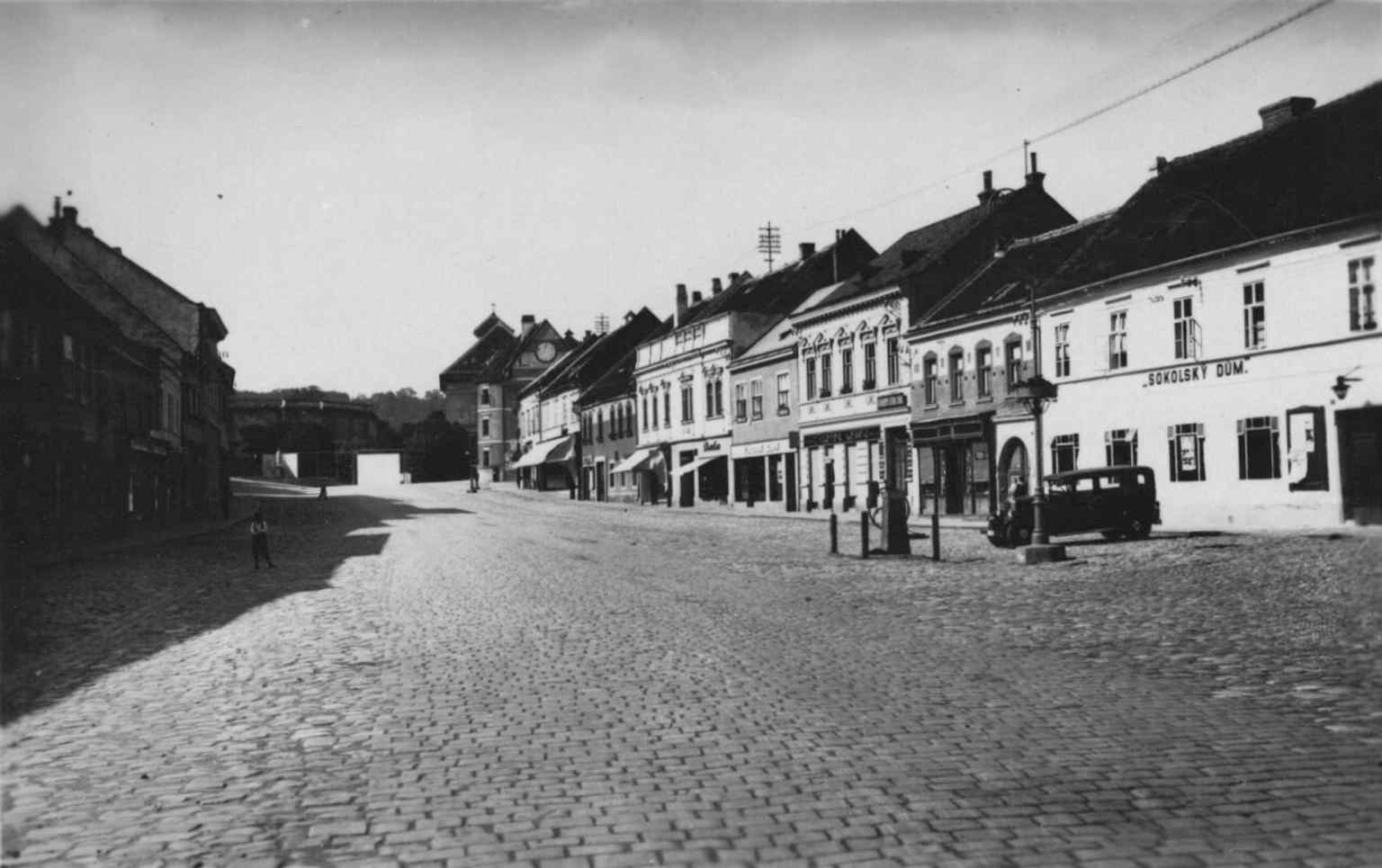 This 1930 view from the south shows the sloping Palackého náměstí, with the Sokolský dům (later Hotel Napoleon) on the right and the castle stables and Neoclassical church in the distance.
