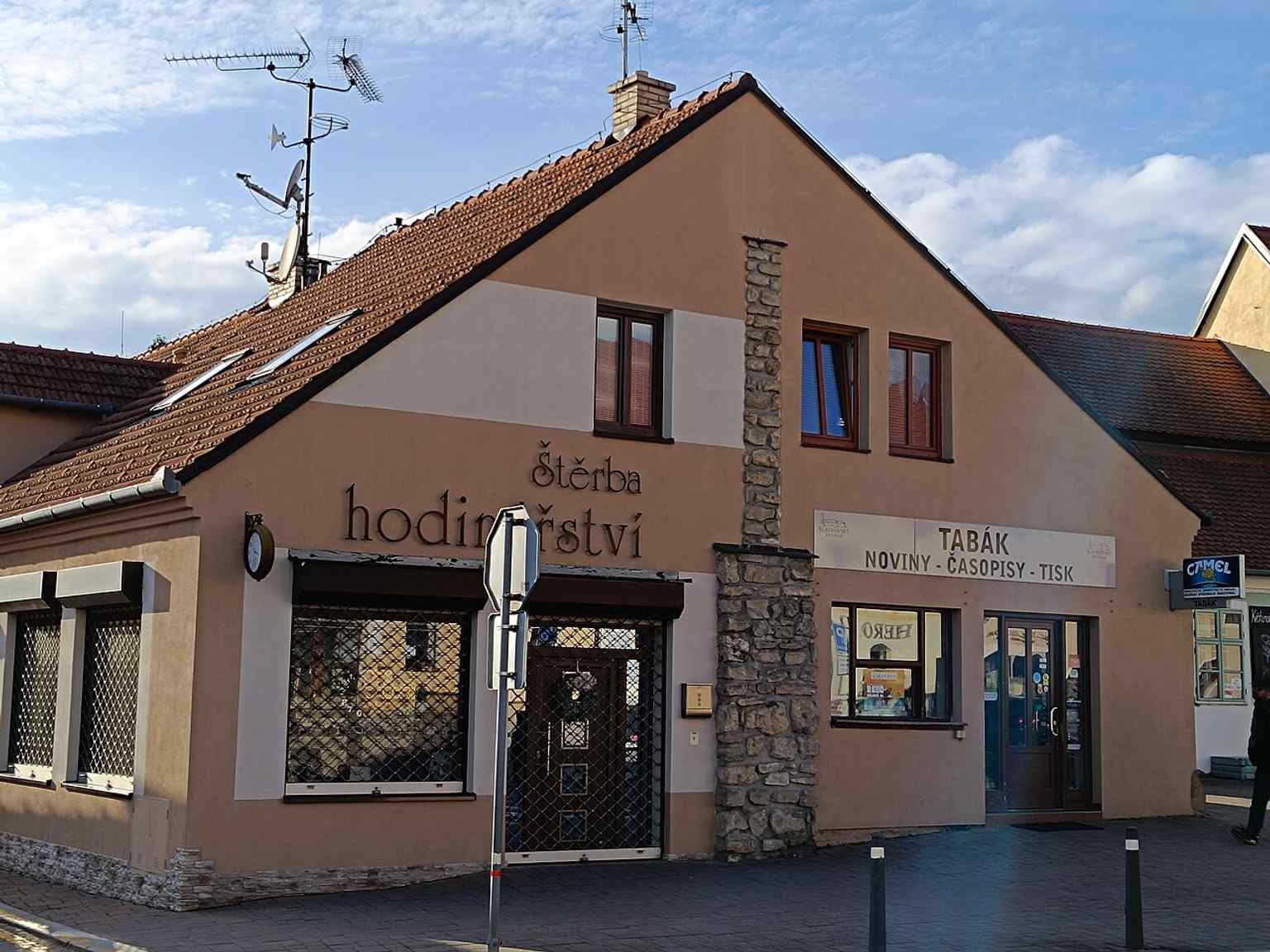 This modern photo shows houses 79 and 278 at the southern end of Palackého náměstí, where the Hodinová brána once stood, with a symbolic marking indicating the former medieval city fortifications.