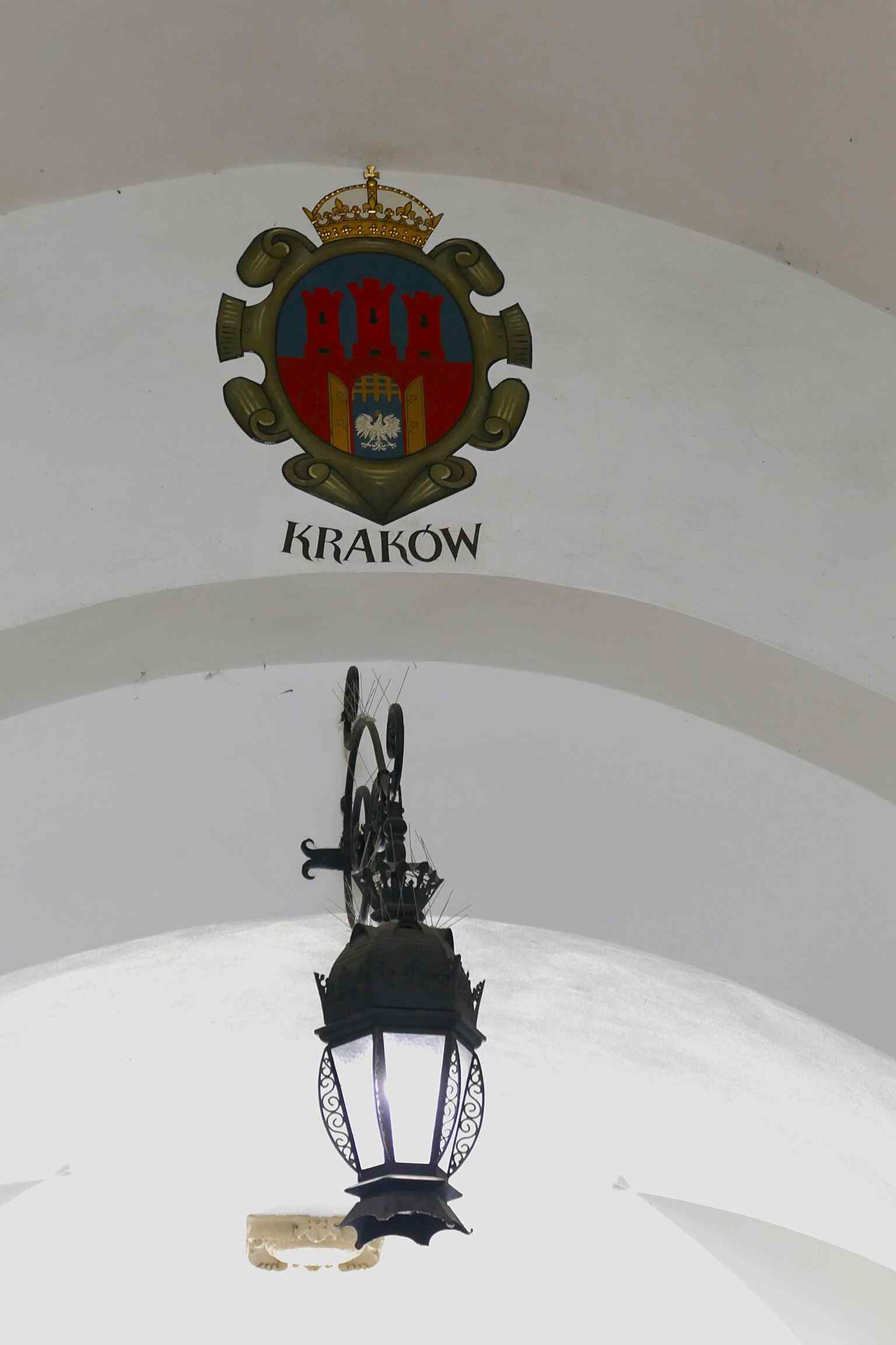 The Kraków coat of arms detail inside Sukiennice, one of the civic symbols installed when the lower hall became a row of wooden stalls.
