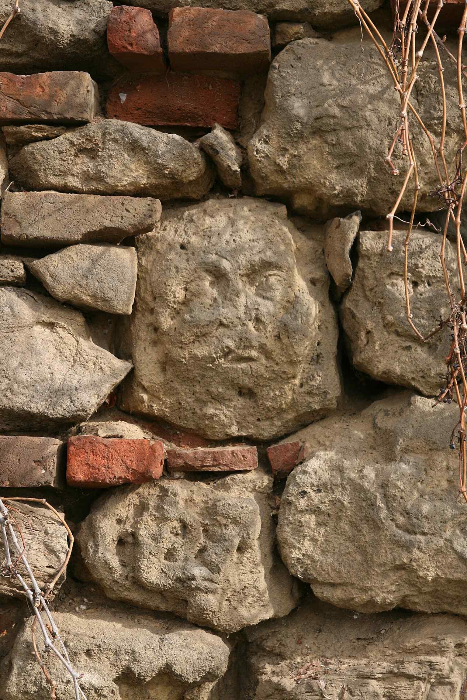 A close-up reveals one of the unique faces carved into the stones of the city fortifications, an intriguing detail found in the Kollárova street section.