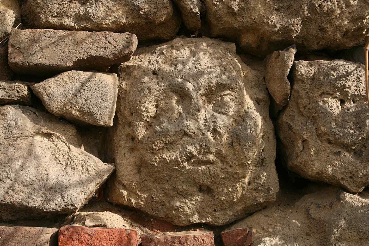 A clear close-up of a single carved face embedded in the stones of the Kollárova street fortifications, an ancient decorative element.