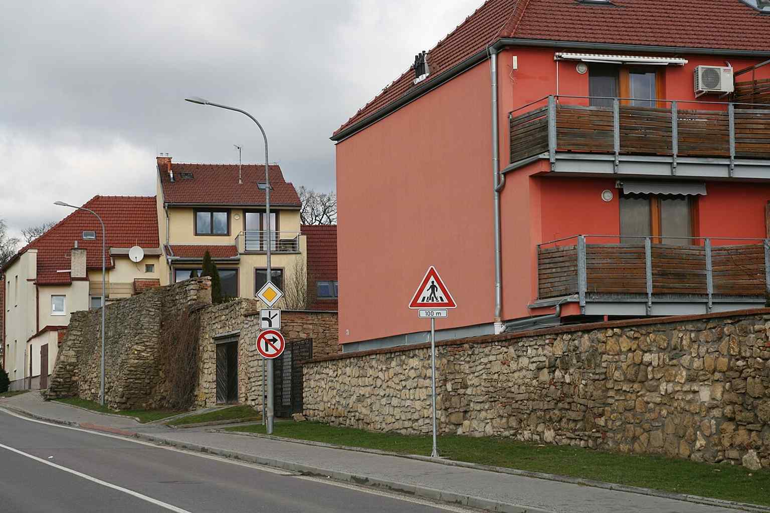 This image shows the medieval city wall in Kollárova street, with residential buildings integrating into its structure and a view towards the junction with Brněnská Street, highlighting its urban context.