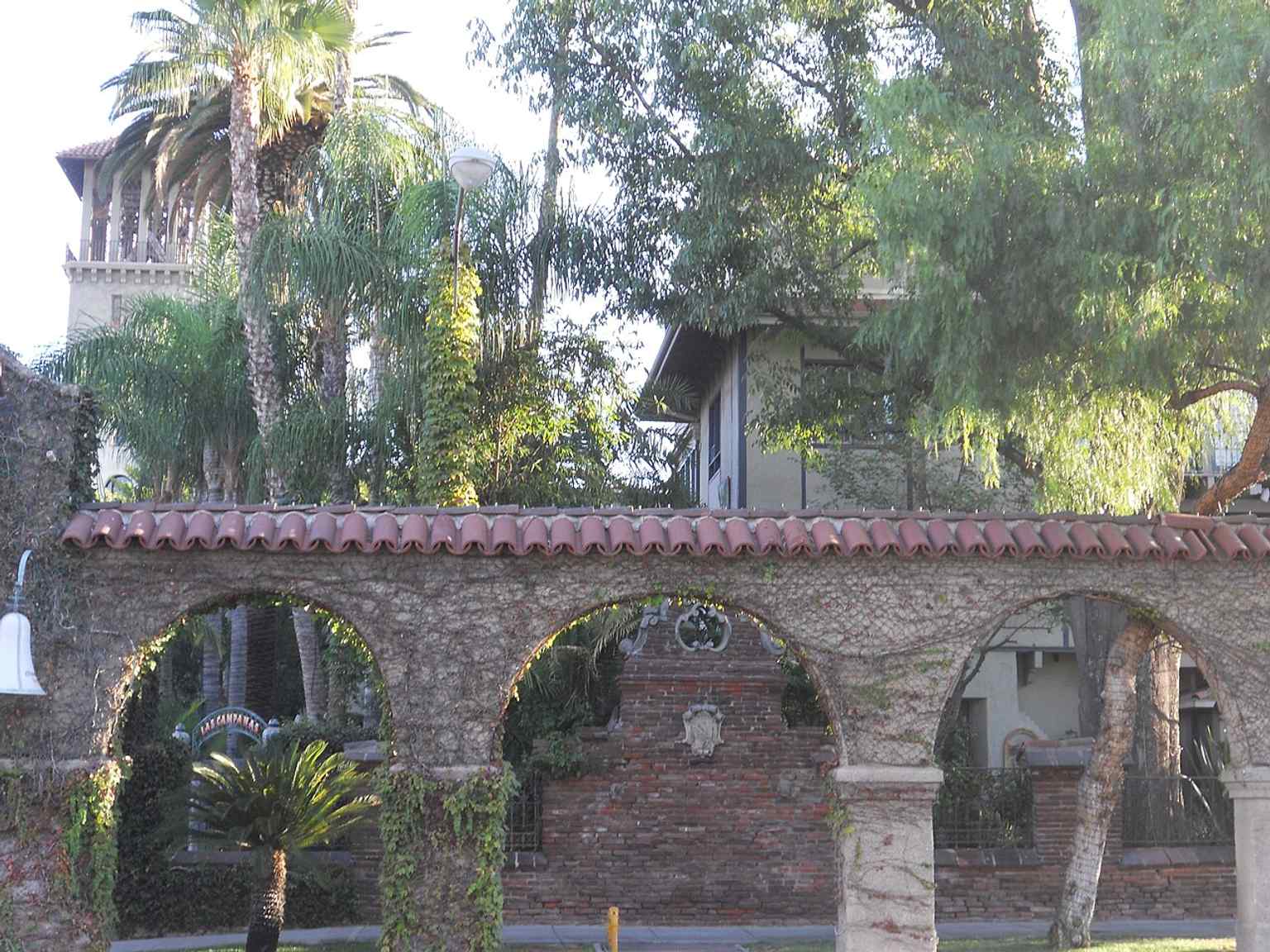 The front walkway arches show the inn’s layered Mission Revival styling and narrow passageways mentioned in its eclectic design.