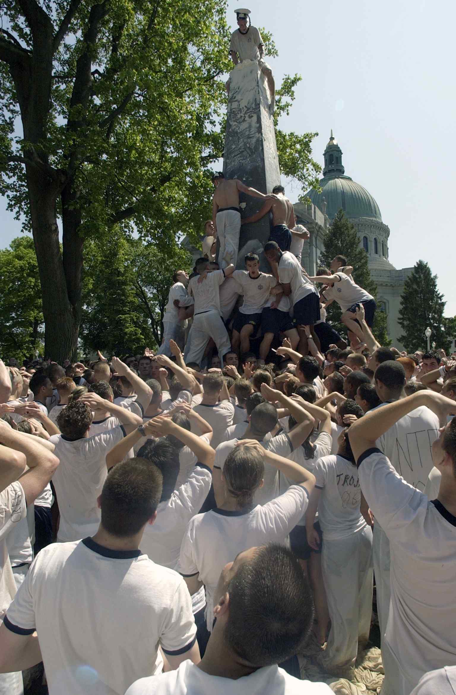 Midshipmen attempt to climb the Herndon Monument, famously covered in over 200 pounds of lard, a tradition reinstated in 2011 to foster spirit and camaraderie among the plebes.