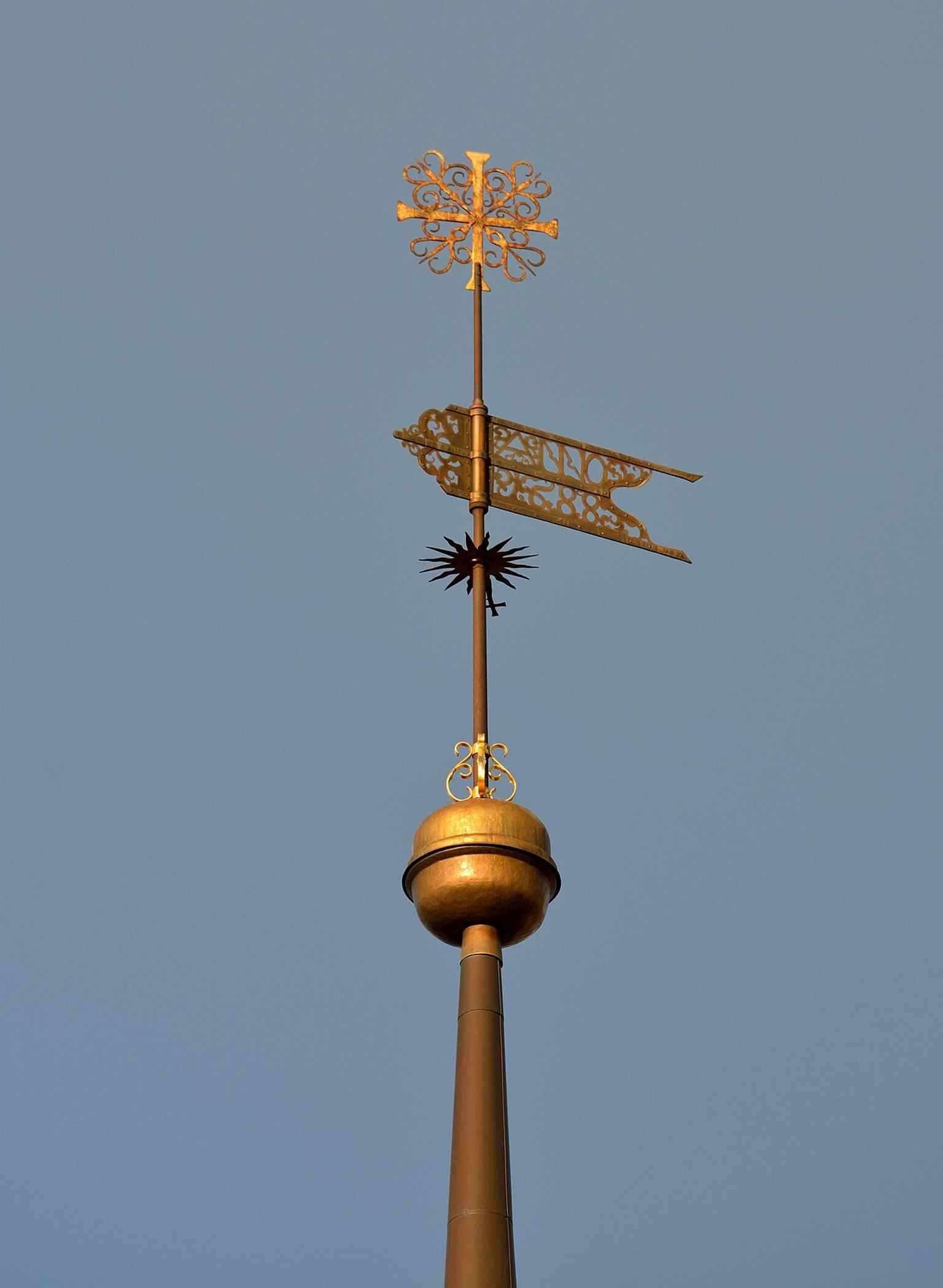 The tower’s finial and weather vane, recalling the 1688 restoration after the 1684 fire and the church’s rebuilt spire silhouette.
