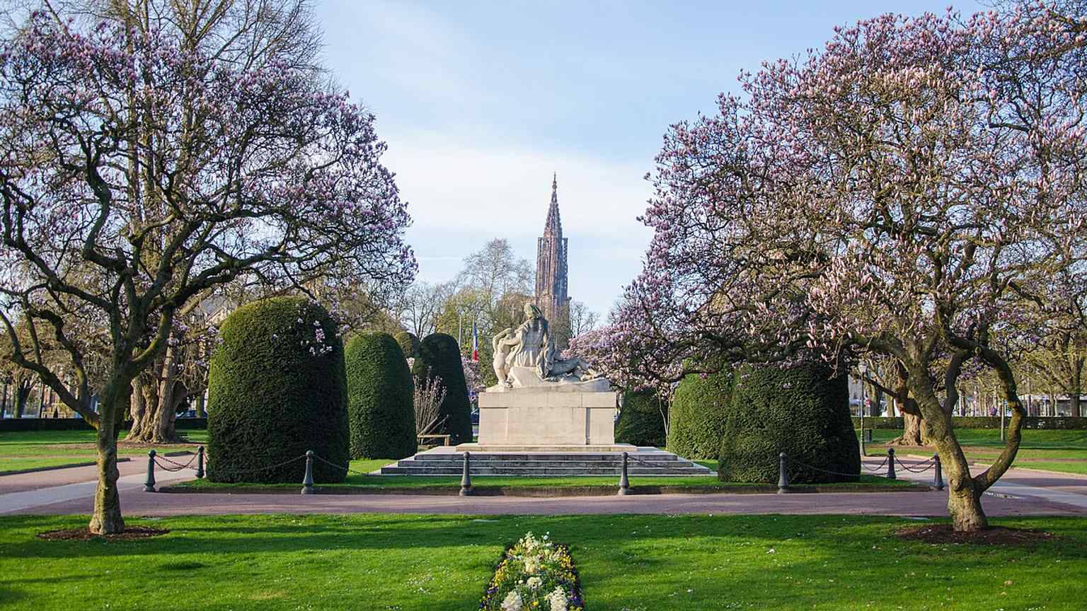 A symmetrical view centered on the war memorial and its planting beds, echoing the square’s carefully designed monumental layout.