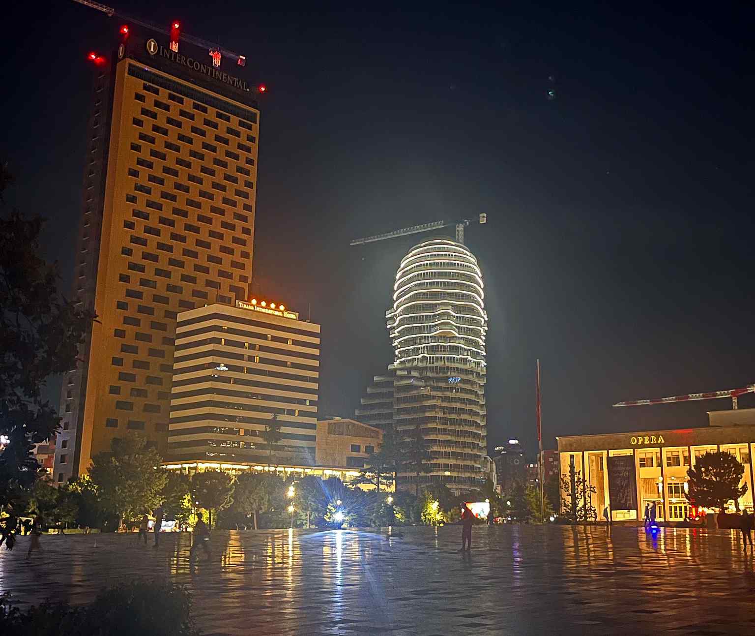 See the Palace of Culture, home to the National Theatre of Opera and Ballet, illuminated at night in Skanderbeg Square, where its first stone was symbolically placed by Nikita Khrushchev in 1959.