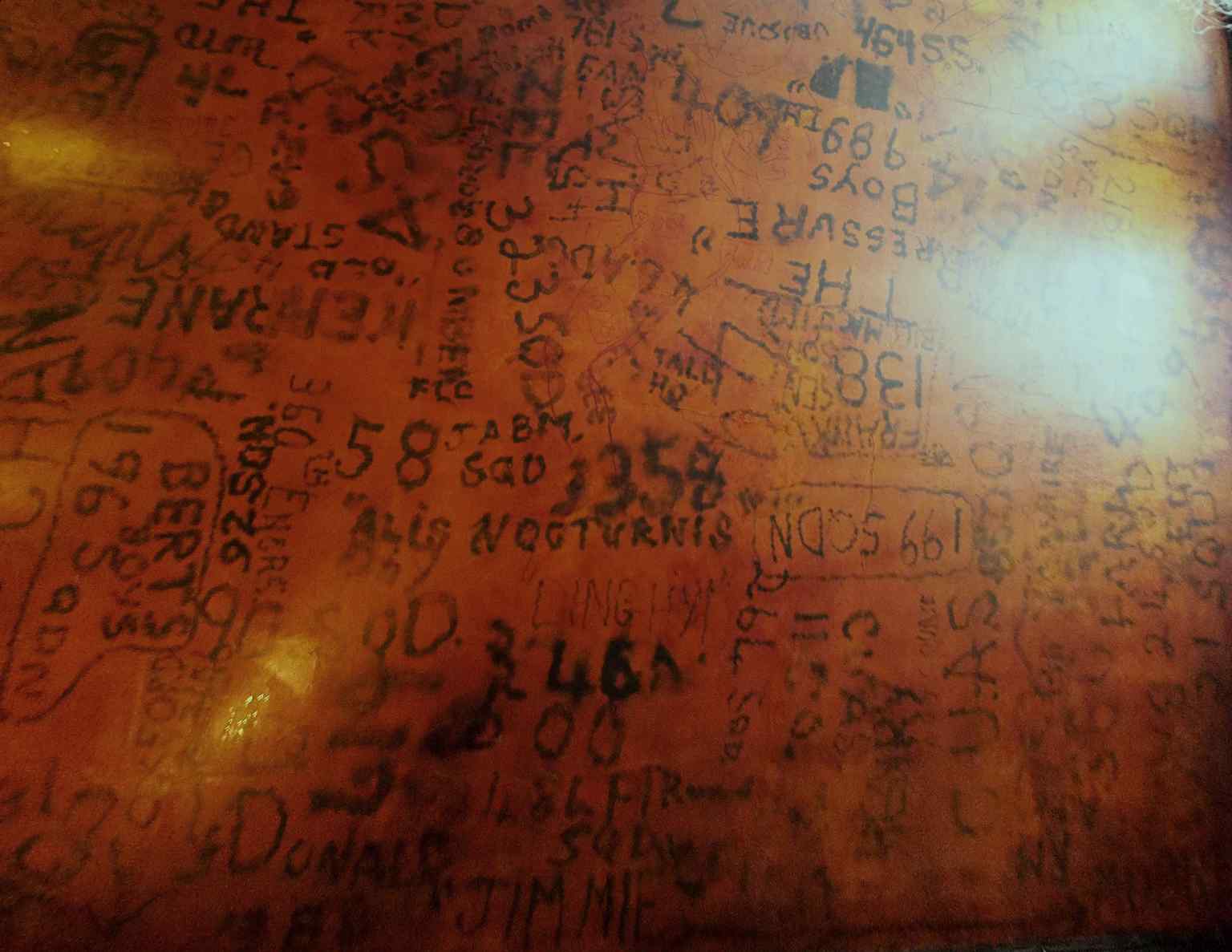 A closer look at the historic RAF Bar ceiling, where Allied airmen left their mark with names, squadron numbers, and even a scandalous doodle of a naked woman.