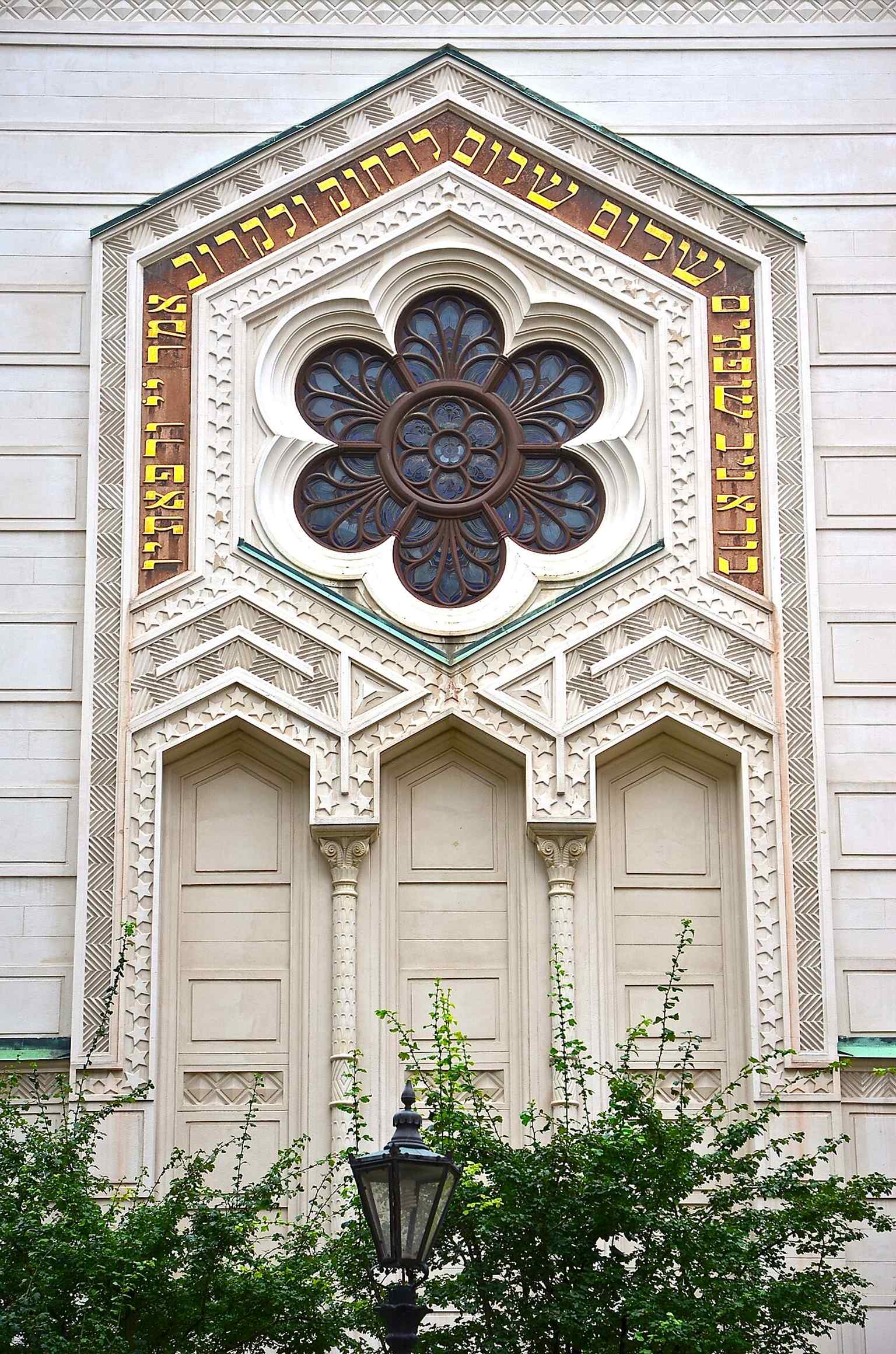 The front facade of the synagogue prominently features the Hebrew inscription from Exodus 25:8-9, 'They shall make a sanctuary for Me, and I will dwell among them.'