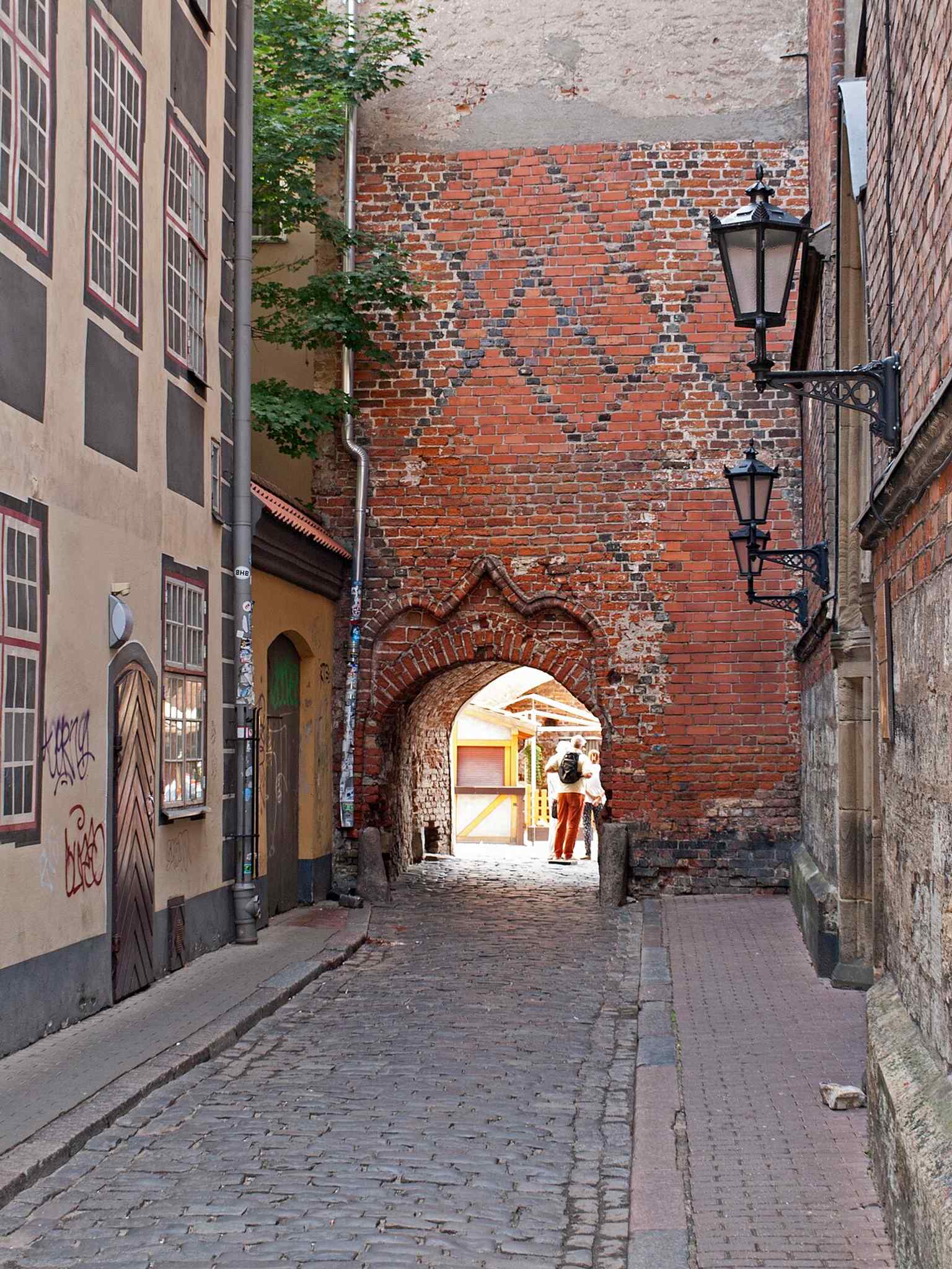 A southwest view into Jāņa sēta, the former Dominican courtyard beside St. John’s Church, still showing the historic passageway that opens into the old complex.