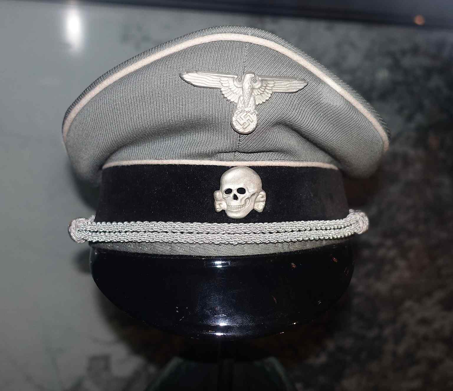 A close view of an SS visor cap, combining the eagle and death’s-head symbols that defined SS uniform design.
