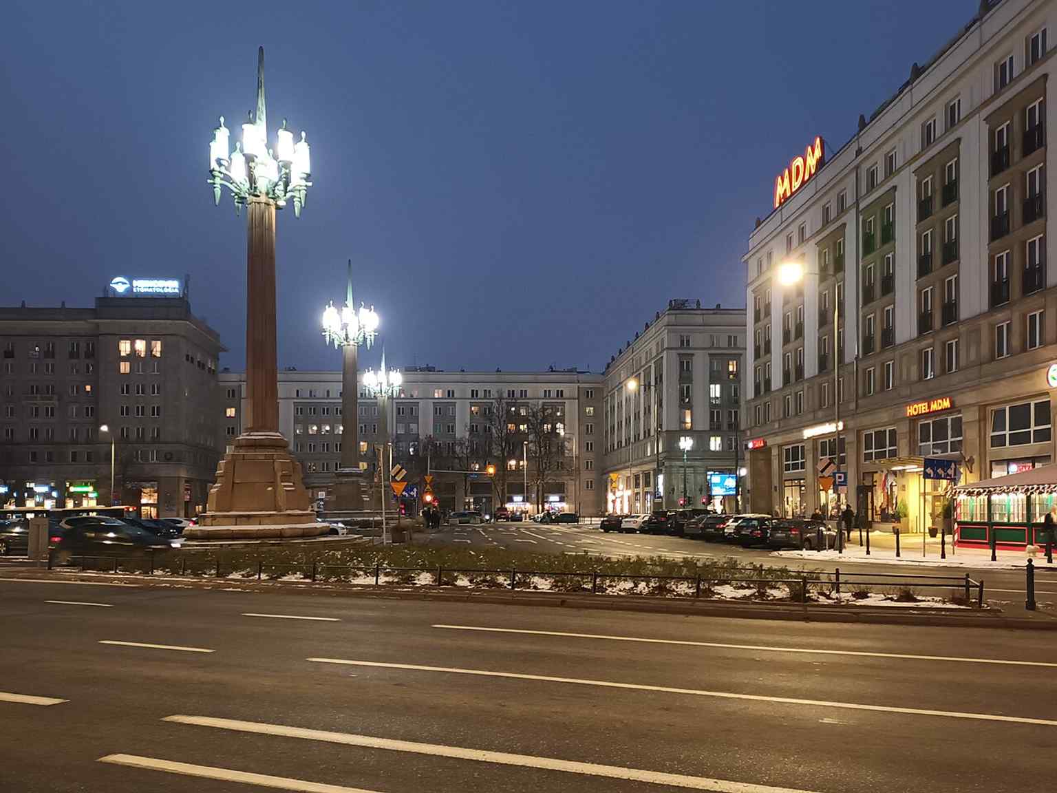 The square at dusk with its three tall candelabra lamps and dense MDM housing blocks.