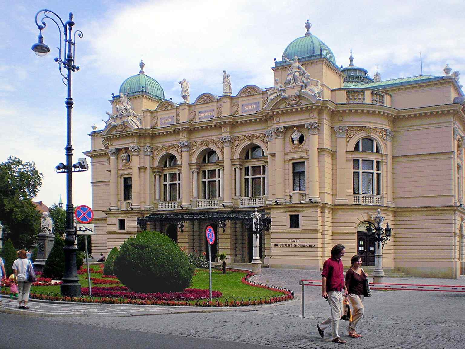 The theatre seen from the Planty side with the Aleksander Fredro monument nearby, matching the landmark’s everyday urban context.