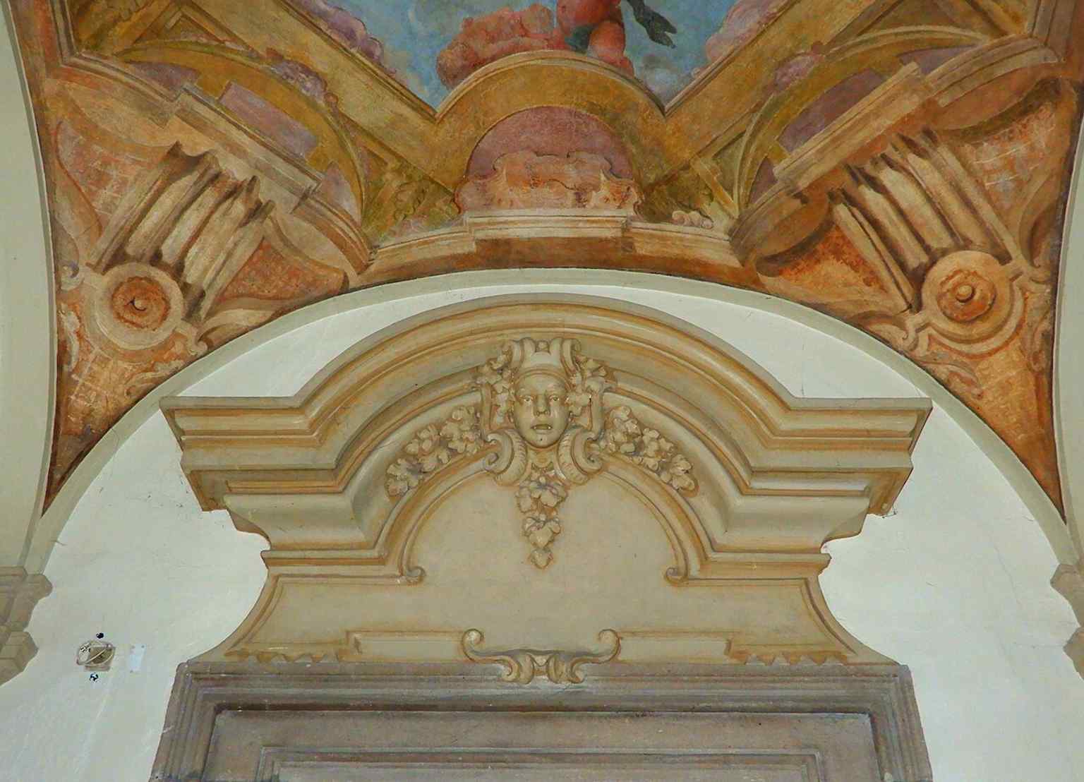 A detail of a supraporta with a mascaron, showcasing the intricate sculptural work associated with Matyáš Bernard Braun's workshop, a master of Prague Baroque art.