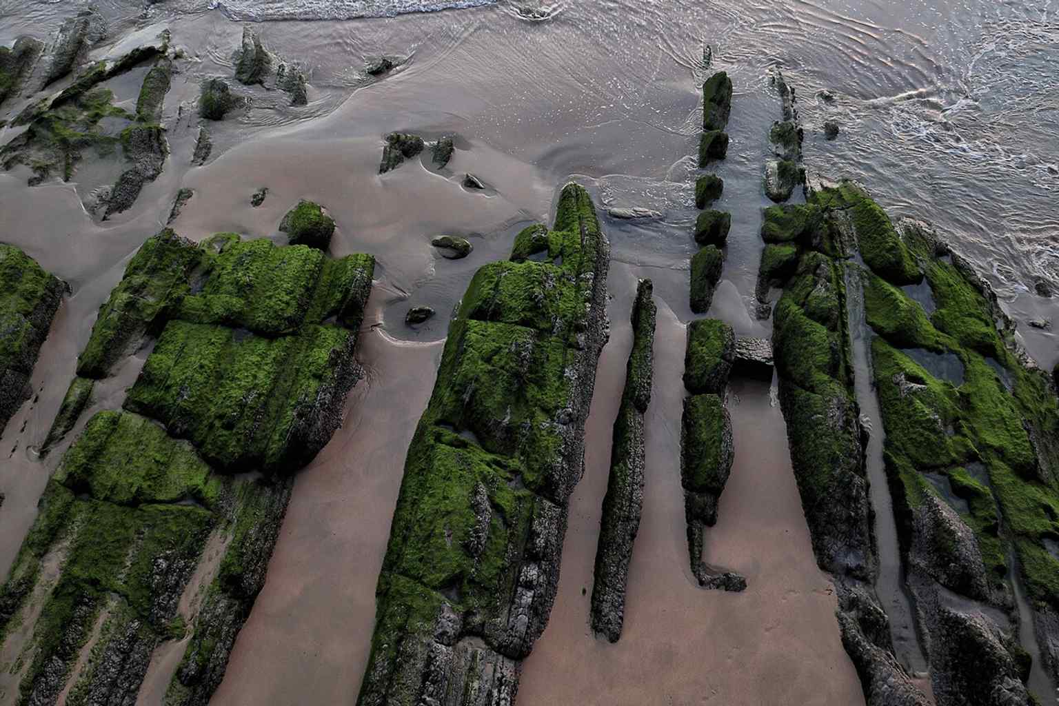 Sunrise over La Concha Beach, highlighting the broad sandy arc and shallow shoreline that changes dramatically with the tide.