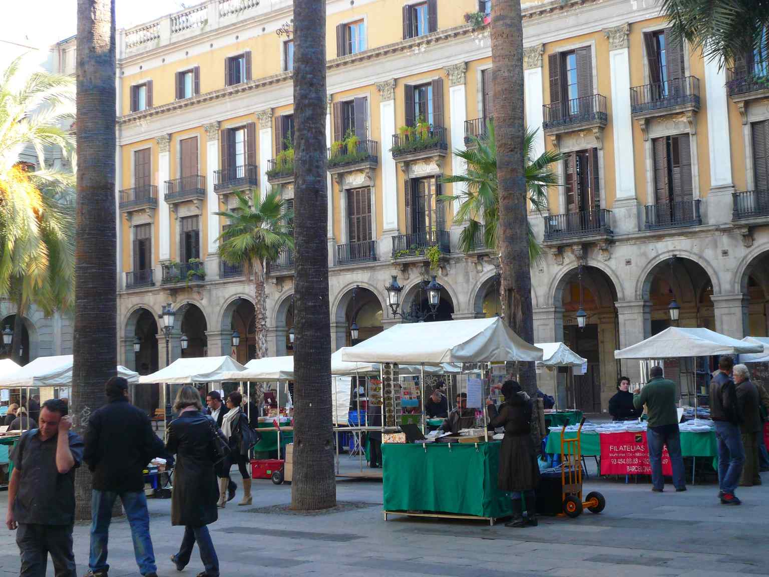 Observe the neoclassical architecture of the Plaça Reial's buildings, designed by Francisco Daniel Molina, featuring ground-floor porticoed galleries and Corinthian pilasters on the upper levels.