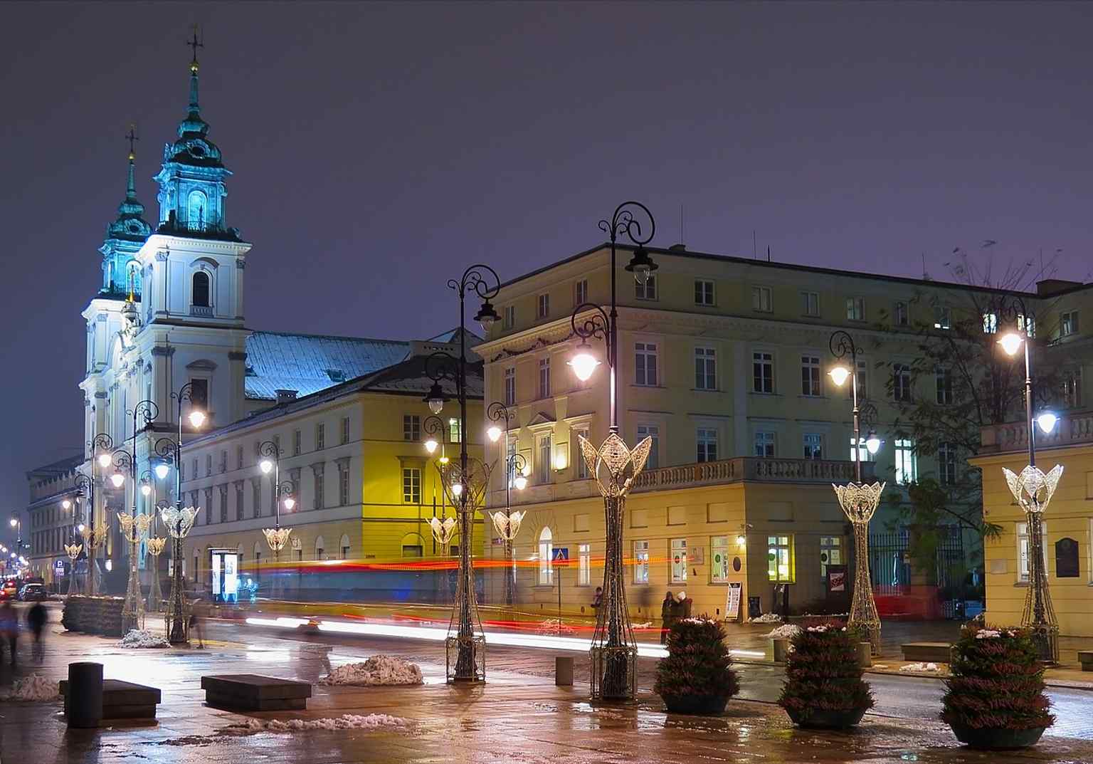 Holy Cross Church lit at night, showing the monumental silhouette that still anchors central Warsaw after centuries of upheaval.