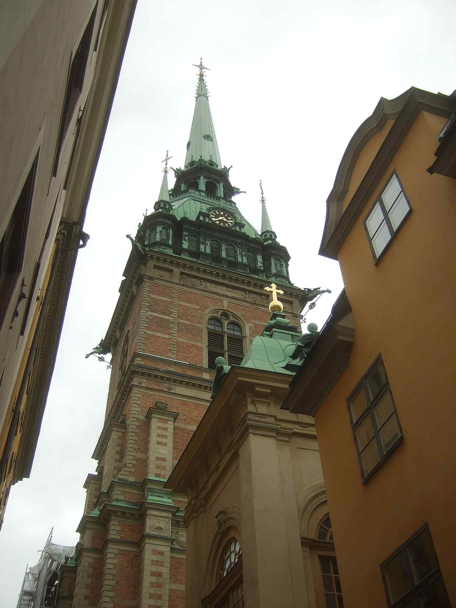 Seen from the busy corner of Tyska Brinken and Västerlånggatan, matching the church’s historic place in the narrow Old Town streets.