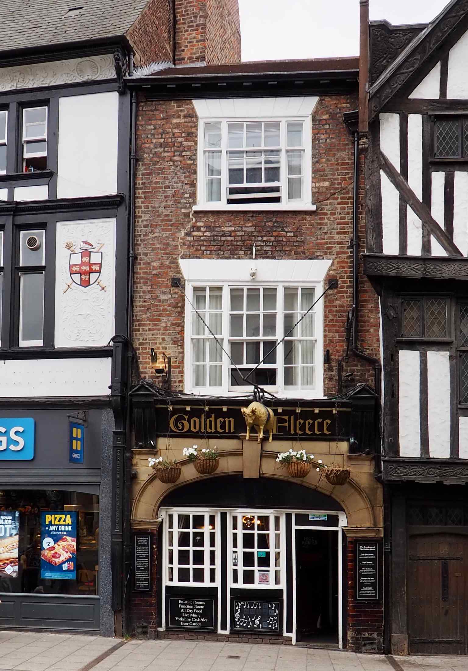 The historic exterior of the Golden Fleece Inn, noted for its pink-grey brick and hanging golden sheep sign (2021).