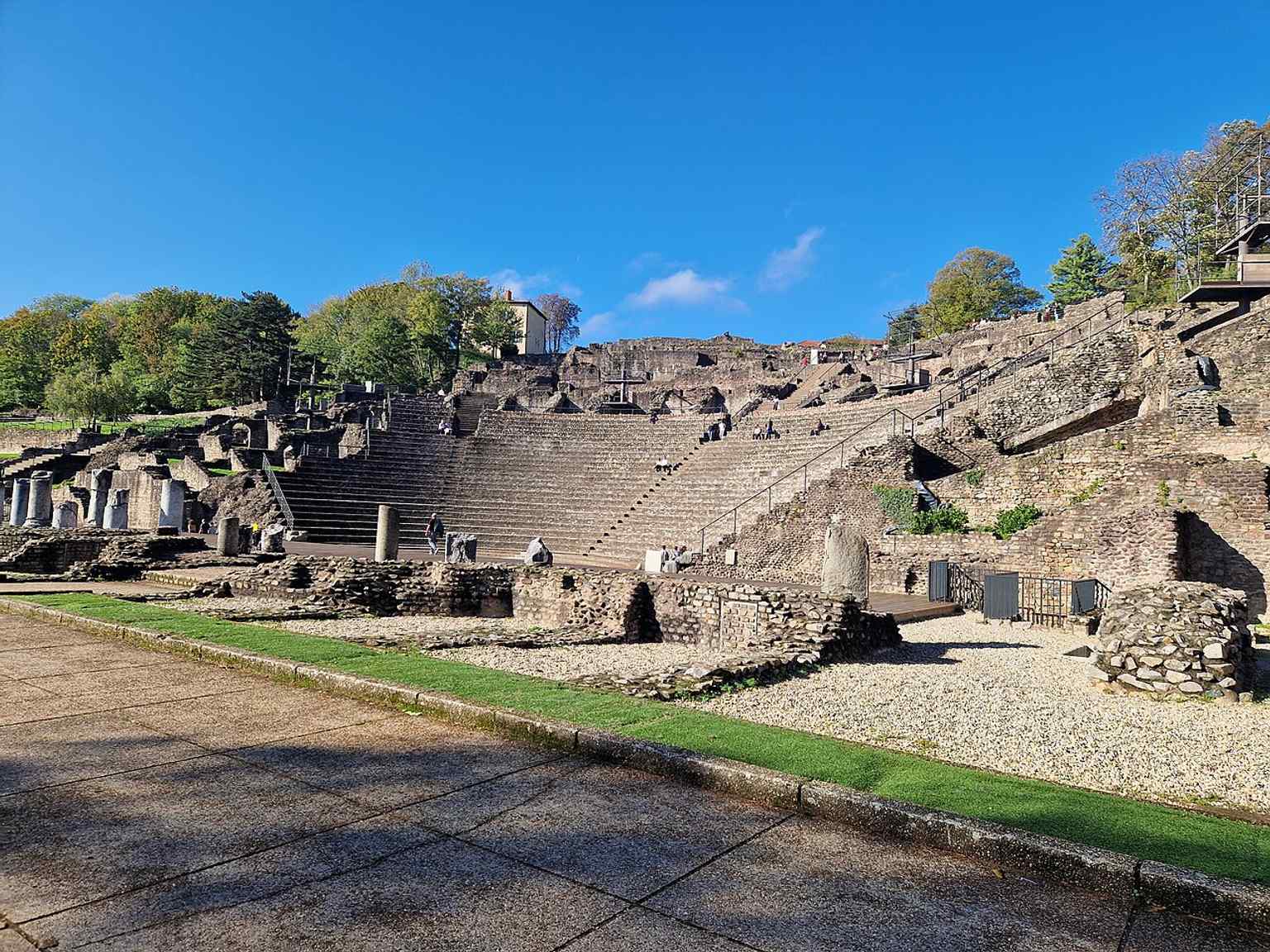 The stage-side view from behind the theatre, useful for seeing the monument’s large Roman structure and how the scene area is set against the hillside.