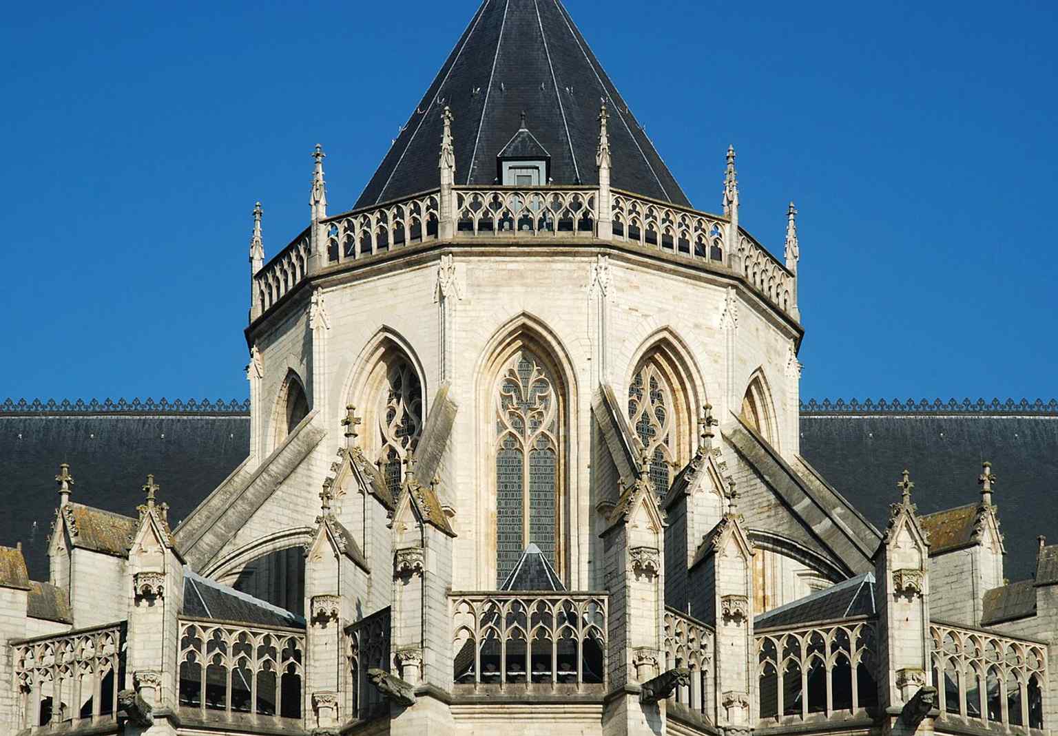 The church’s side exterior emphasizes the soaring Gothic windows and the long, unfinished medieval fabric described in the history.