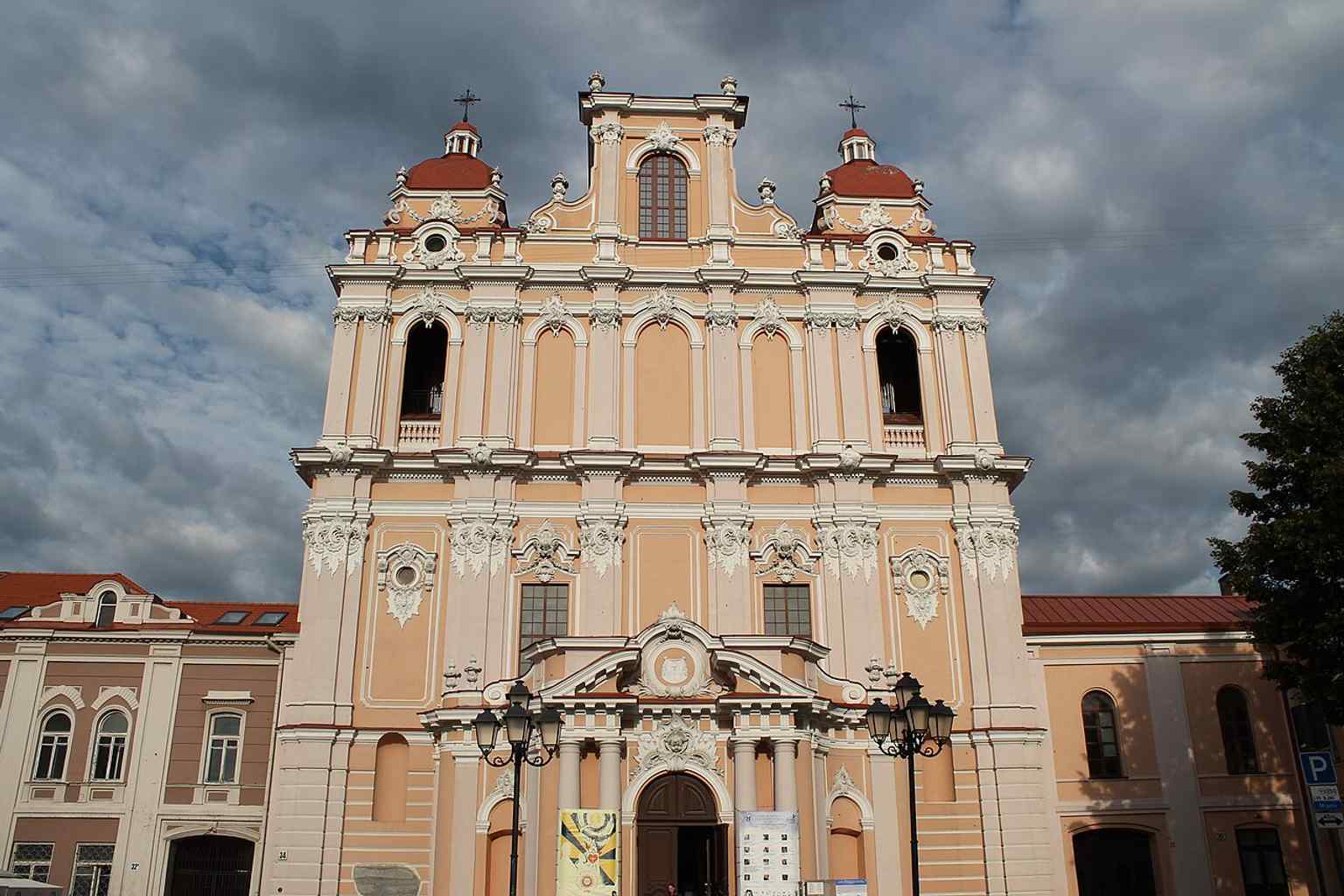 The church framed by trees and sky, showing the distinctive Baroque silhouette that made it a model for later Vilnius churches.