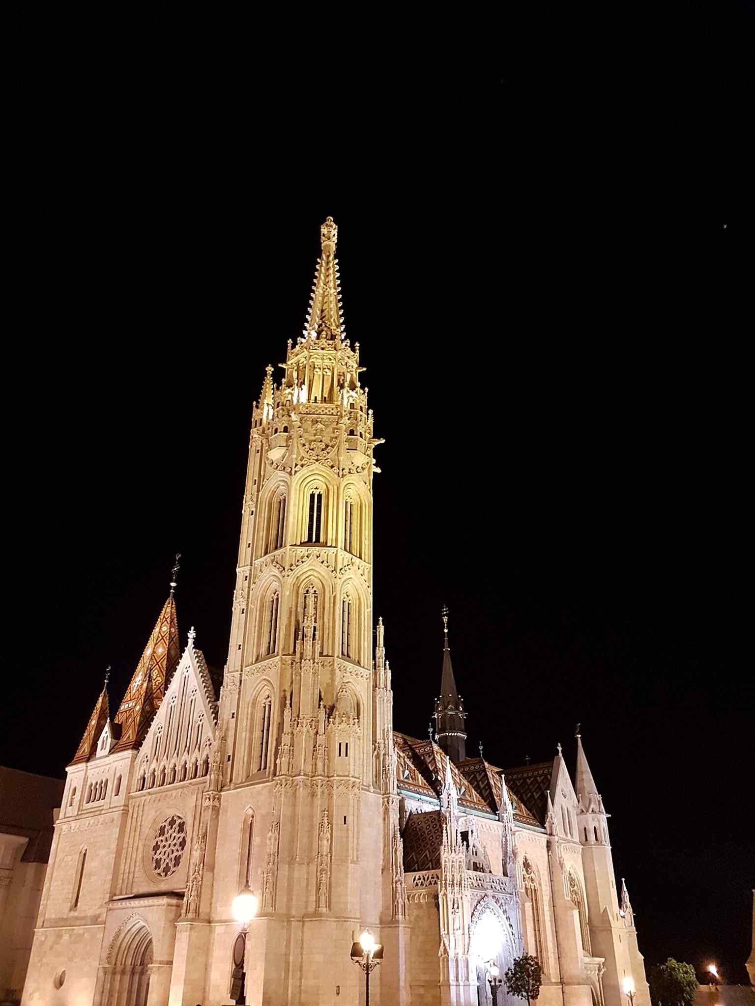 Matthias Church illuminated at night, highlighting its distinctive Neo-Gothic architecture in the heart of Buda's Castle District.