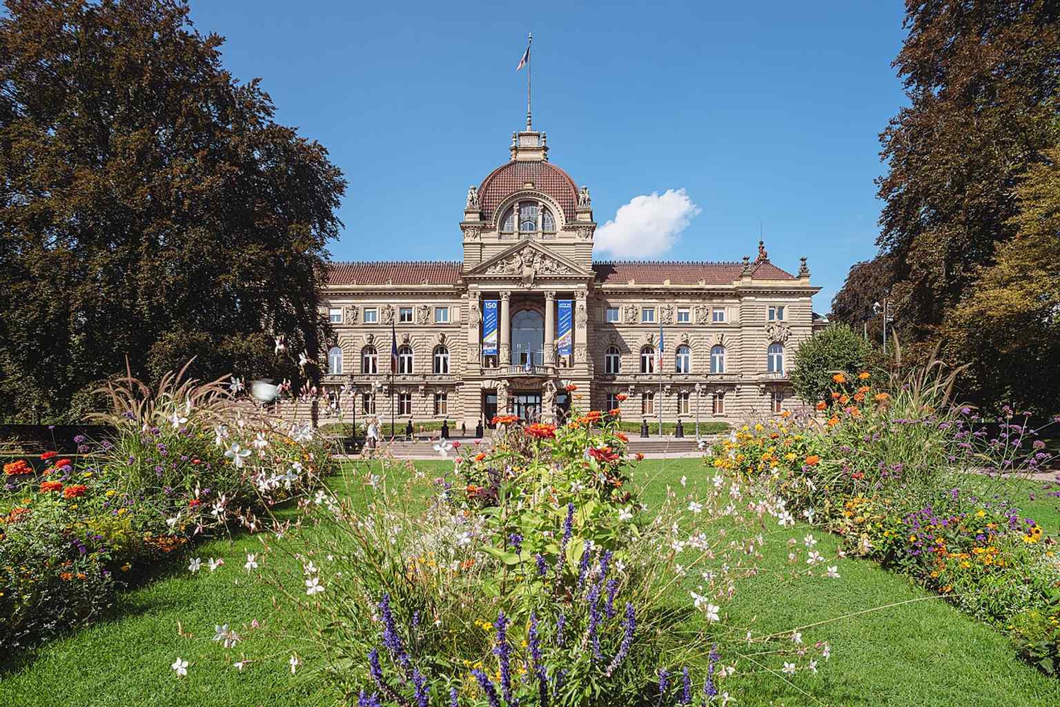 The palace fronted by flowerbeds in the park, a good illustration of the landscaped setting that frames the building.