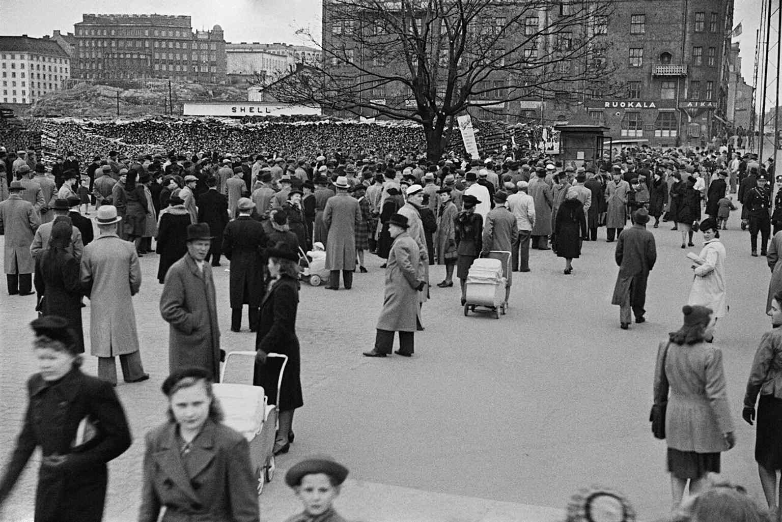 Hakaniemi Market Square crowded in 1946, with wartime firewood stacks still filling the square as the city recovered after the war.