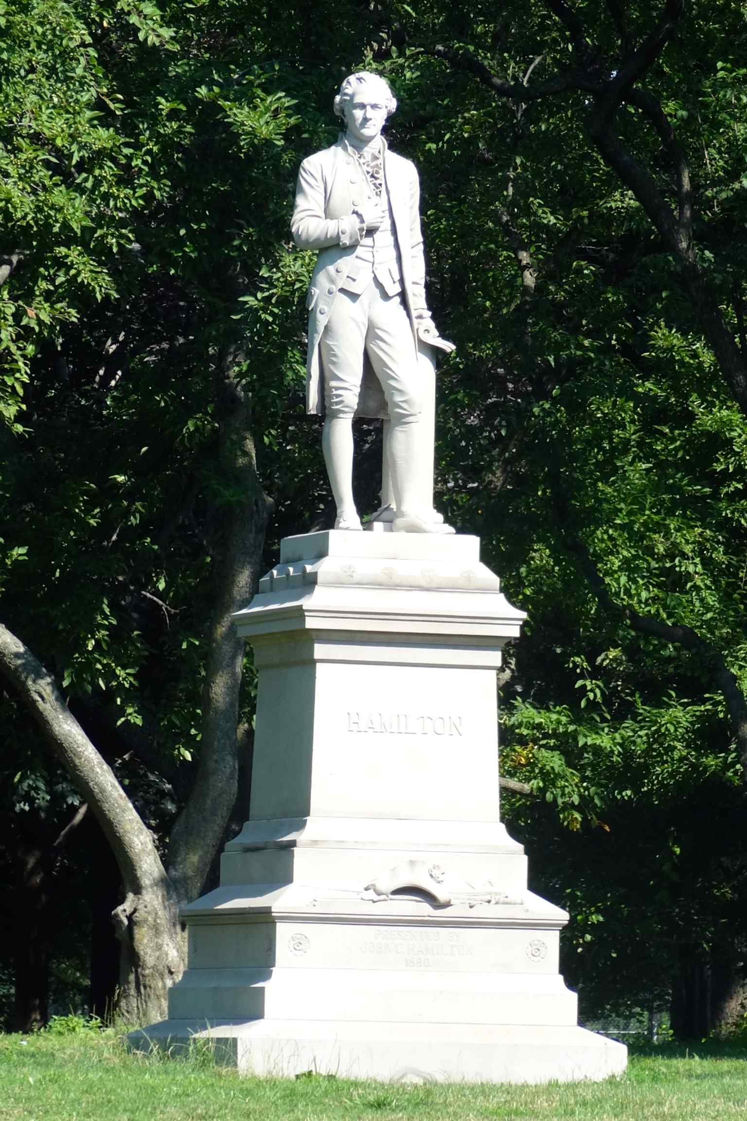A closer angle on Hamilton’s colonial dress and the pedestal, echoing the monument’s commemorative design with the rolled document and formal stance.